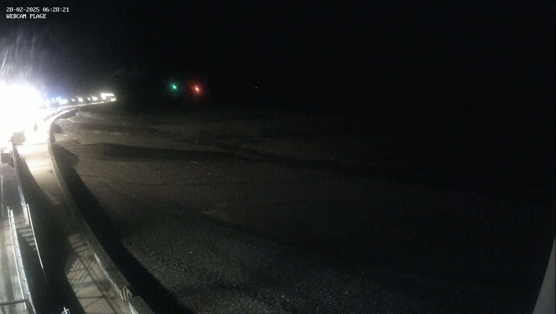 A dark, nighttime scene shows a paved walkway next to a dark, beach-like area under a snowy sky.