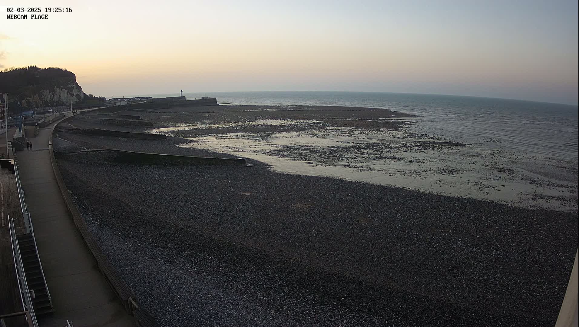 A dark, pebble beach stretches out to a calm sea under a twilight sky.