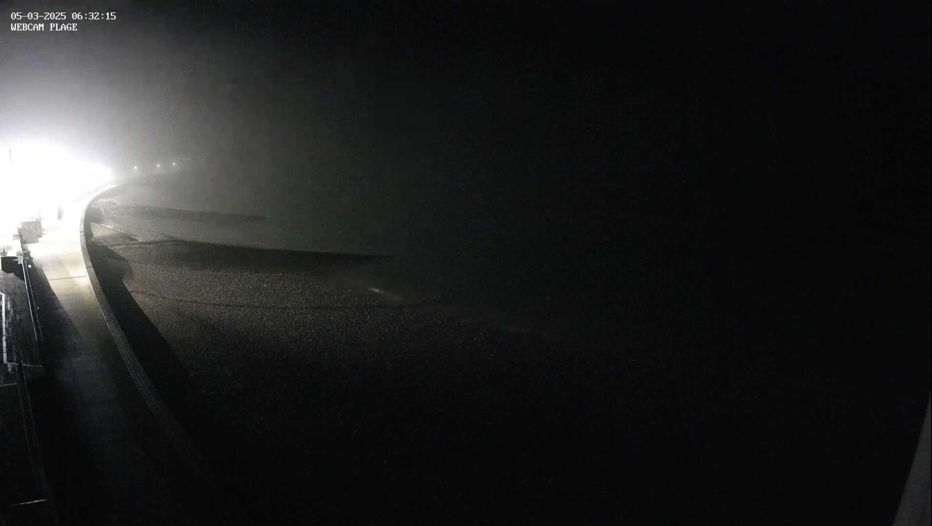 A foggy night scene shows a dark, empty roadway curving to the right, illuminated by distant lights.