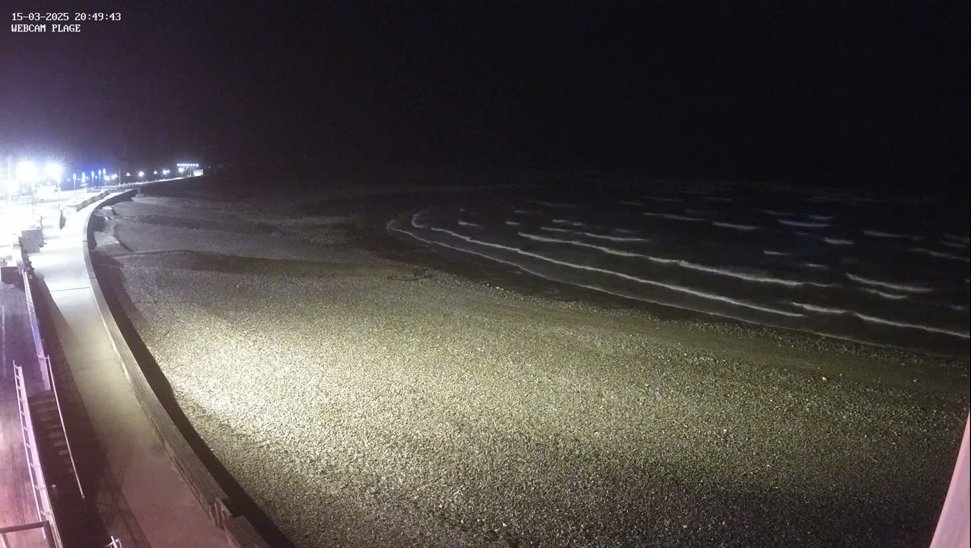A dark, pebble beach at night is gently lapped by small waves under a clear, black sky.