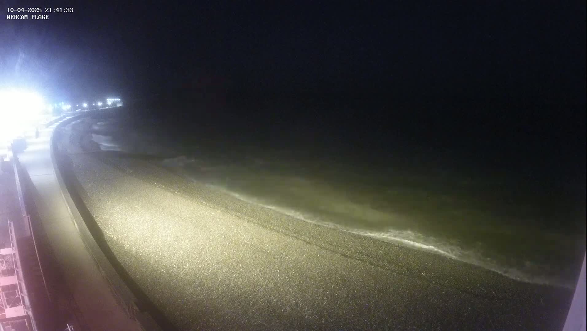 A pebble beach at night with gently lapping waves under a dark sky.