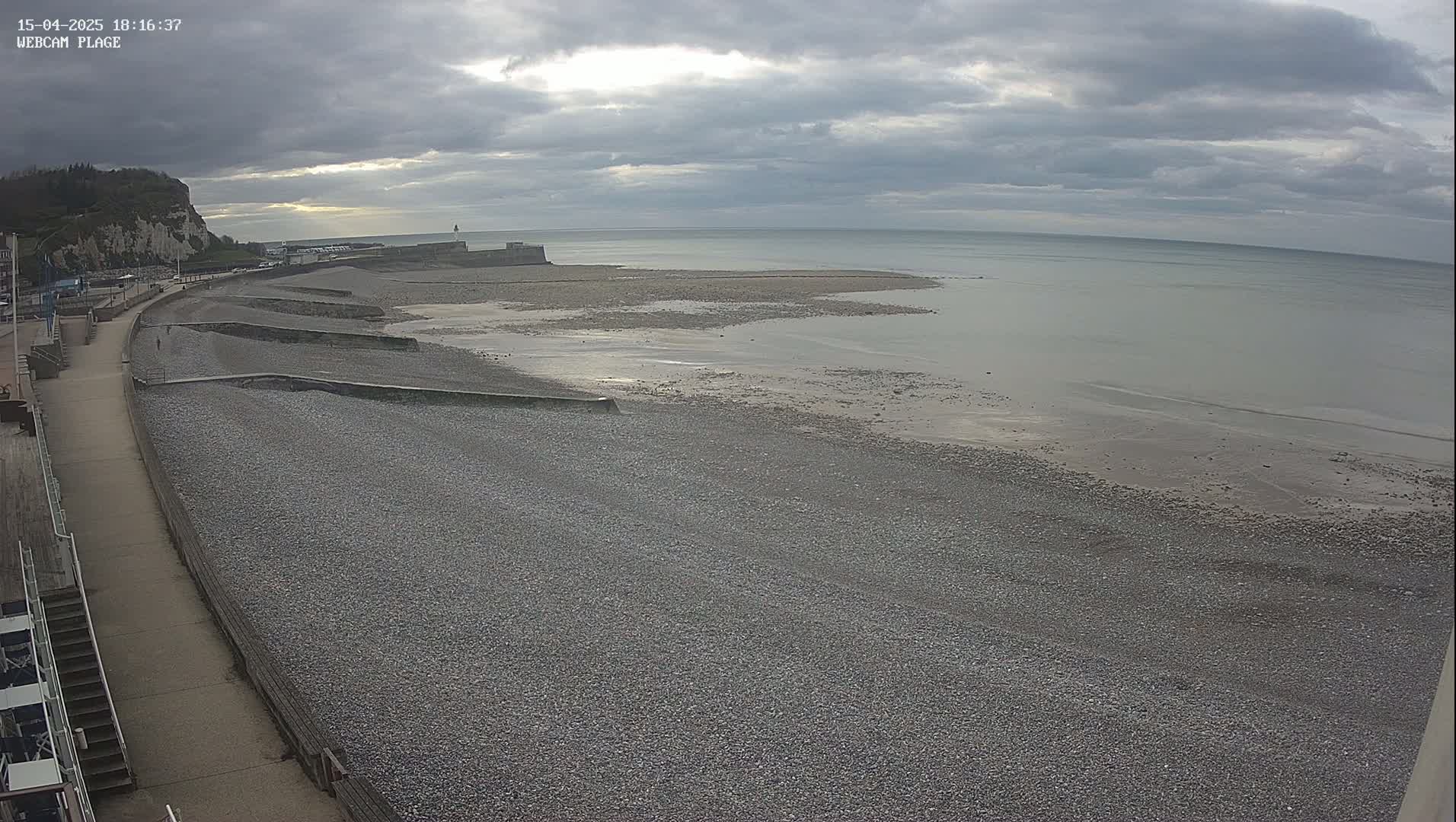 A pebble beach stretches out to a calm, gray sea under a cloudy sky.