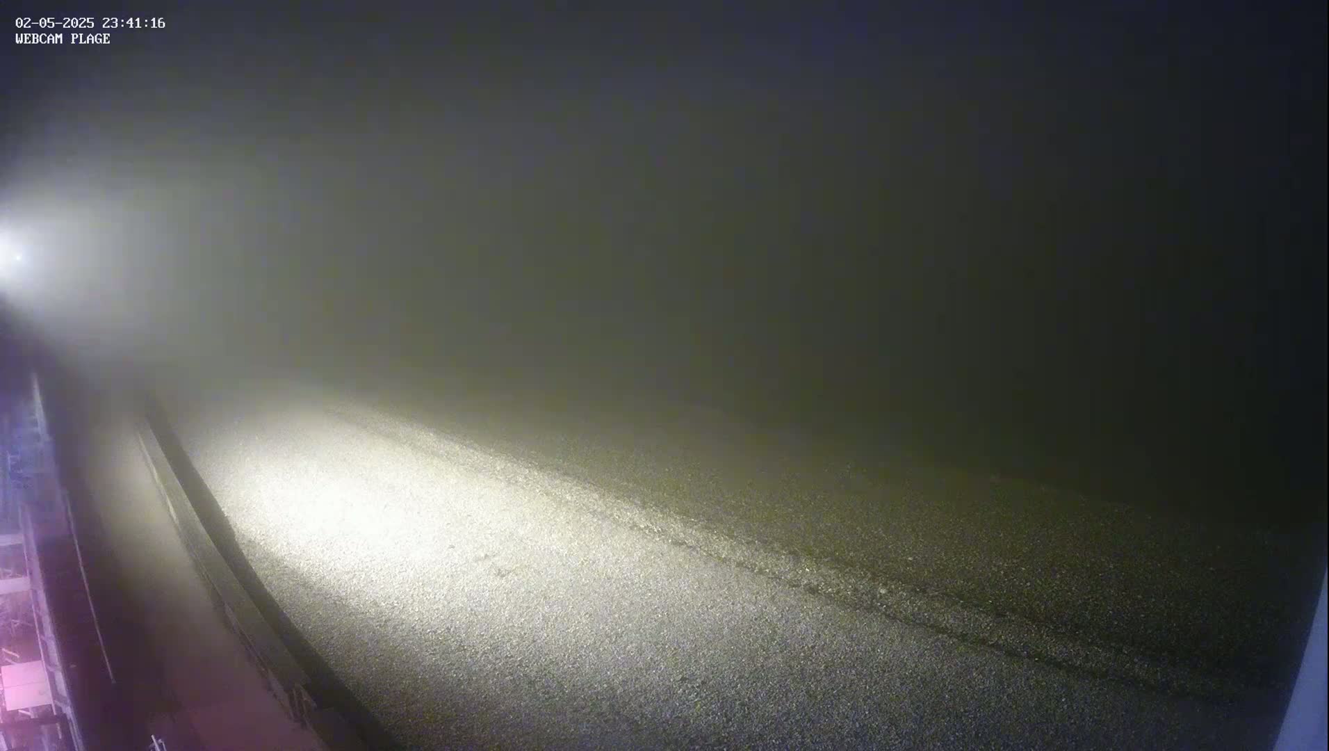 A fog-shrouded road is illuminated by a single light source at night.