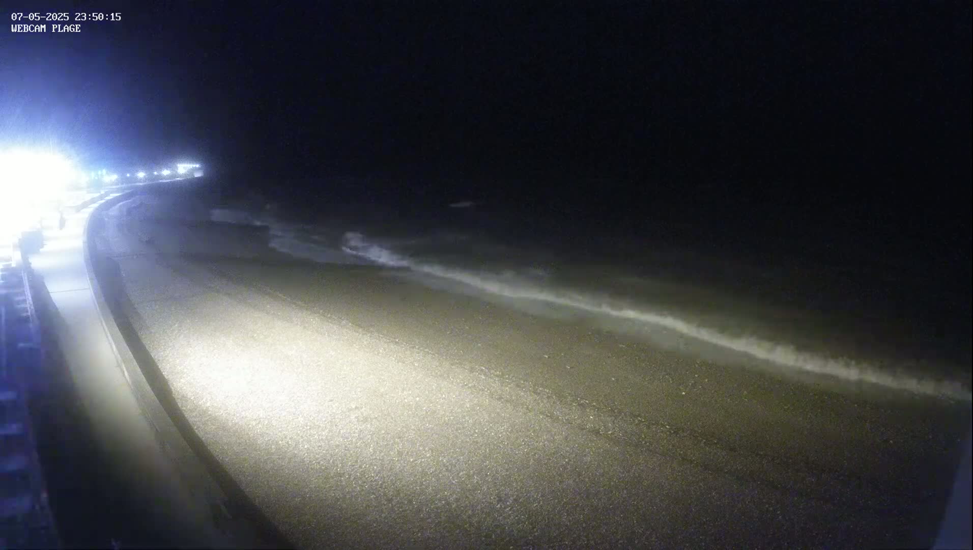 A dark, pebble beach at night is gently lapped by small waves under a clear, black sky.