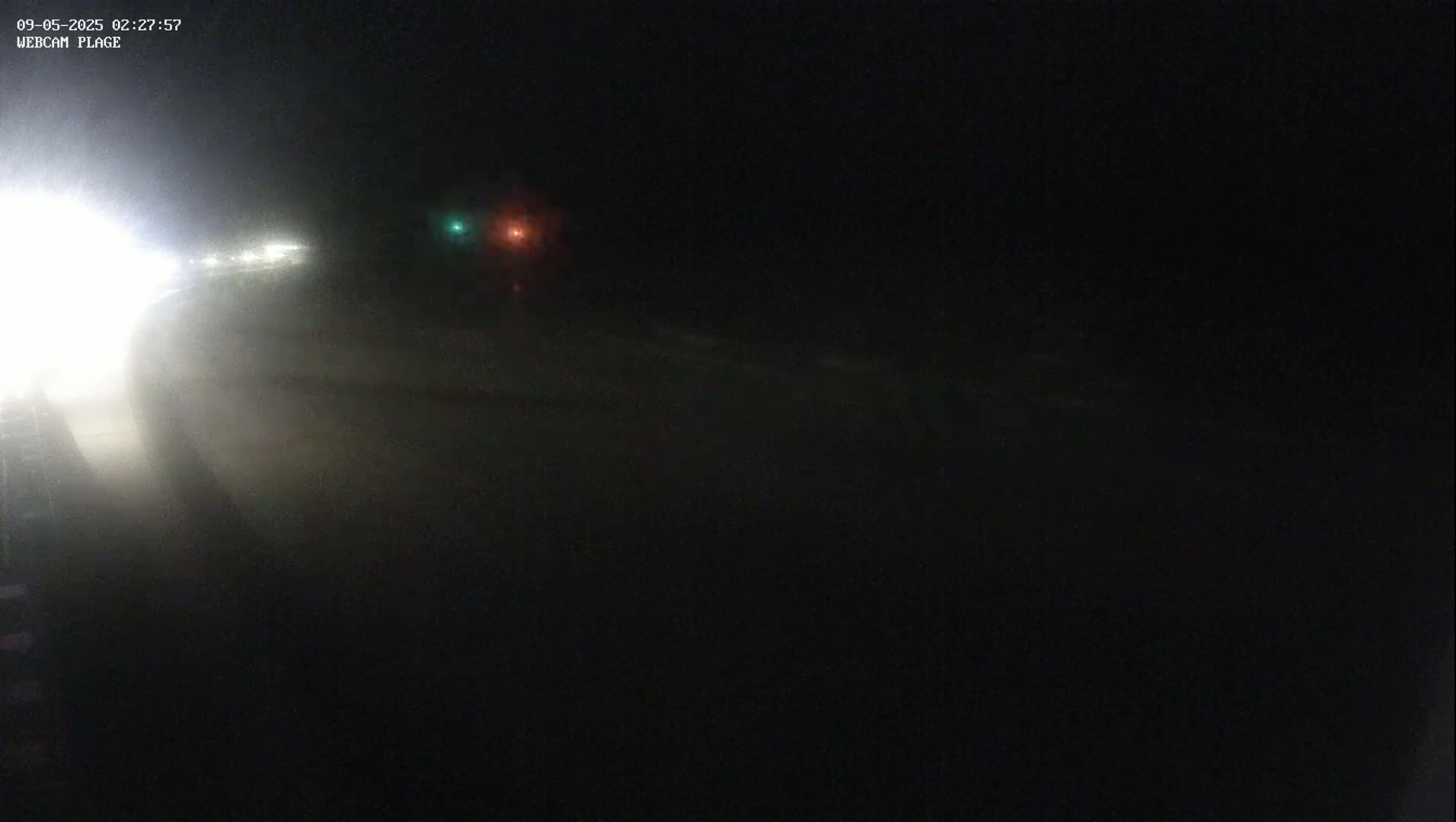 A dark, nighttime scene shows a blurry view of a road with vehicle headlights in the distance, under possibly foggy or misty conditions.