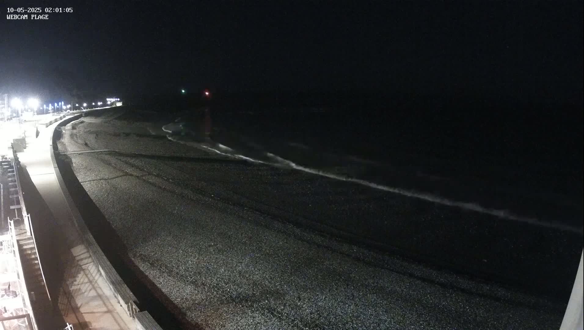 A dark, pebble beach is gently lapped by small waves under a nighttime sky.