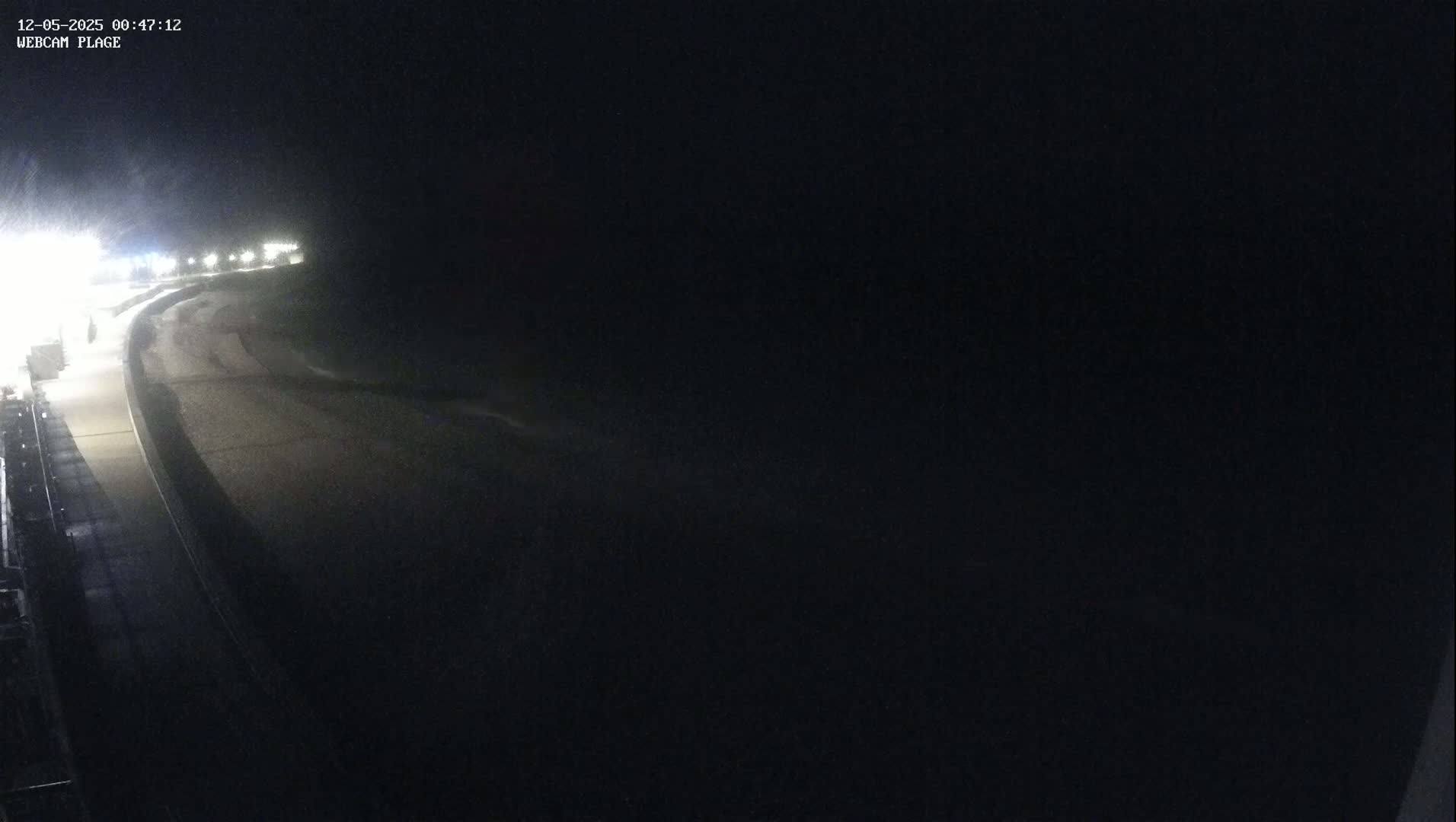 A dark, nighttime scene shows a paved road curving into the distance under a possibly snowy sky, illuminated by distant lights.