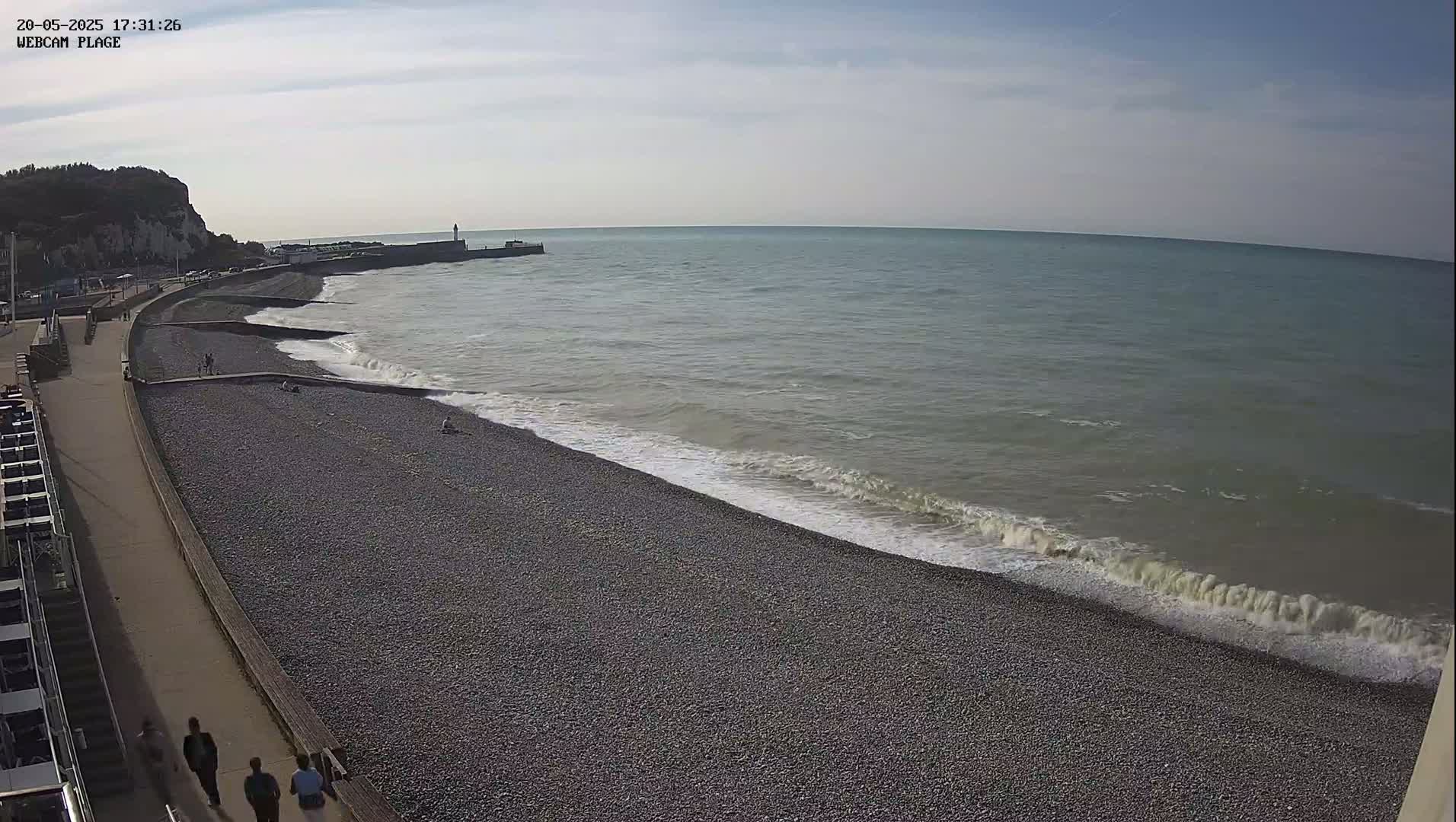 A pebble beach with gentle waves lapping the shore under a partly cloudy sky.