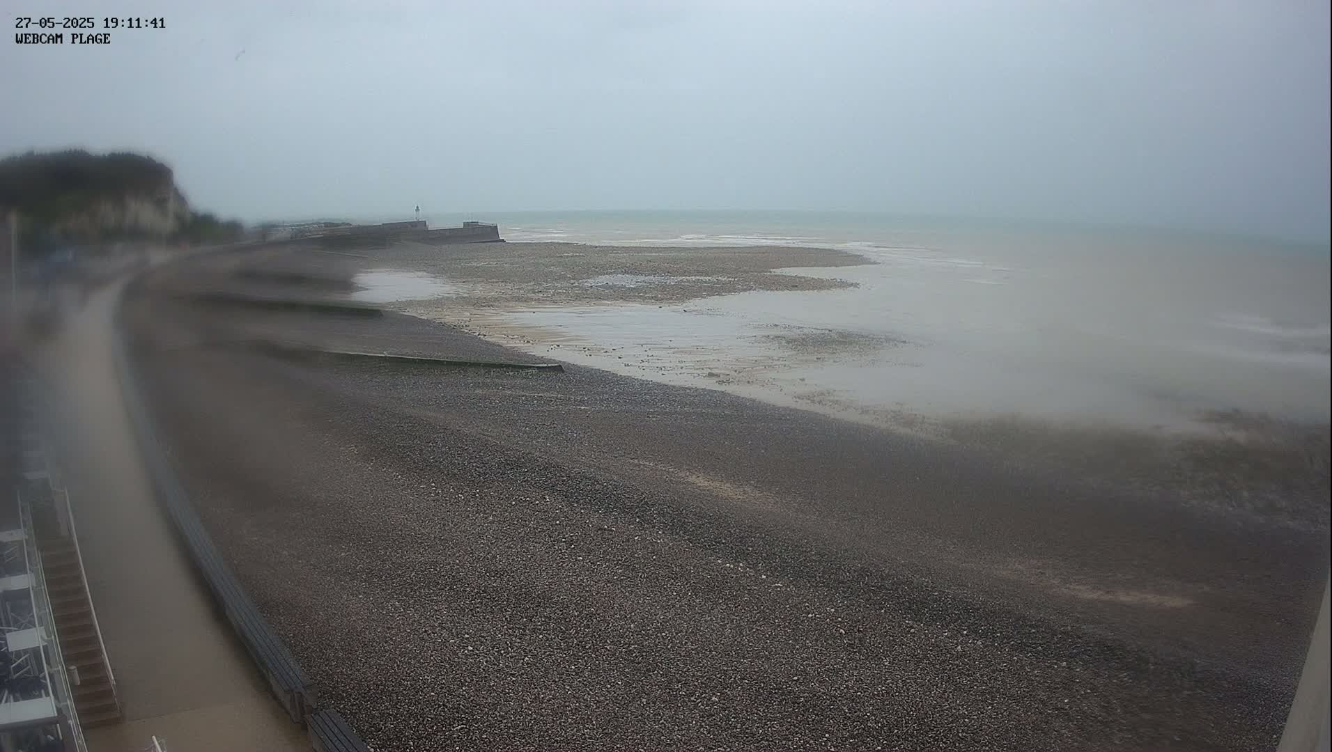 A pebble beach stretches out to a calm, overcast sea under a gray sky.