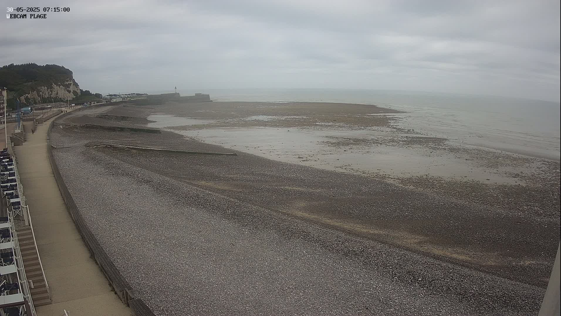 A mostly empty pebble beach stretches out to a calm, gray sea under an overcast sky.