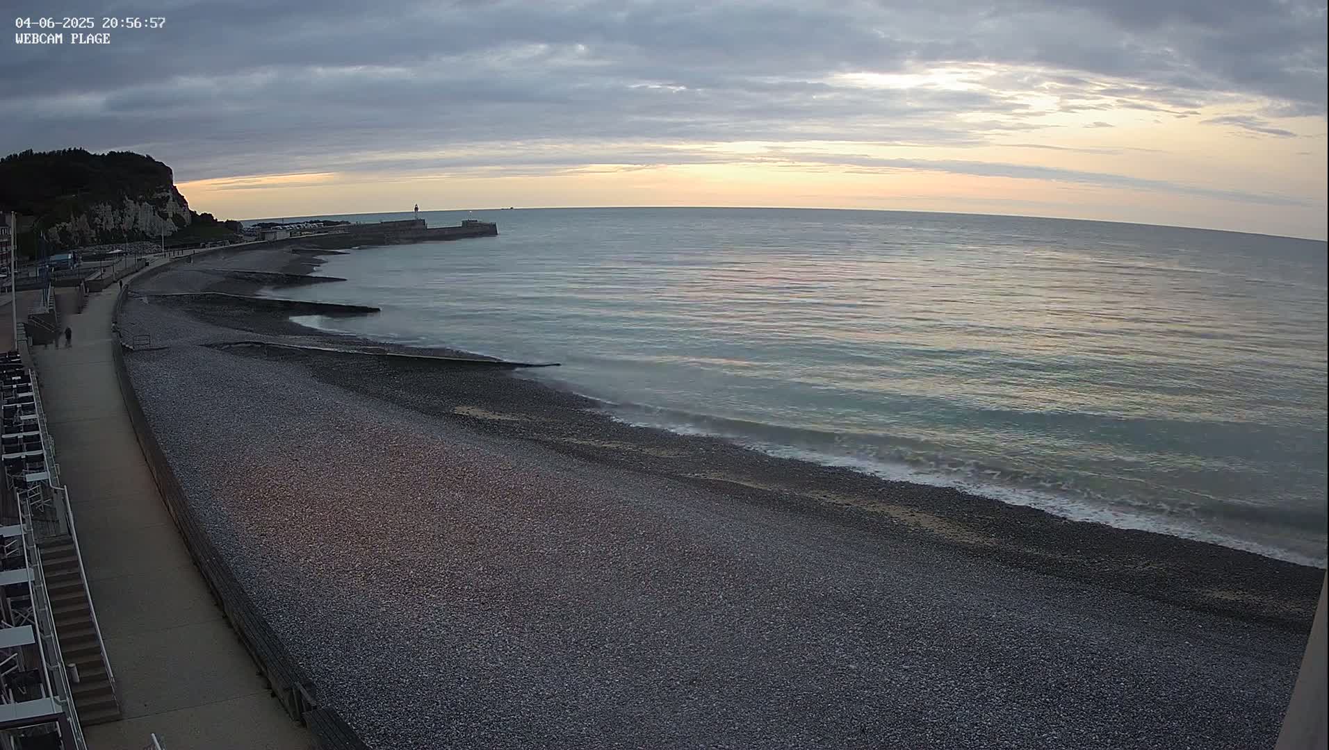 A pebble beach stretches along a calm sea under a partly cloudy sunset sky.