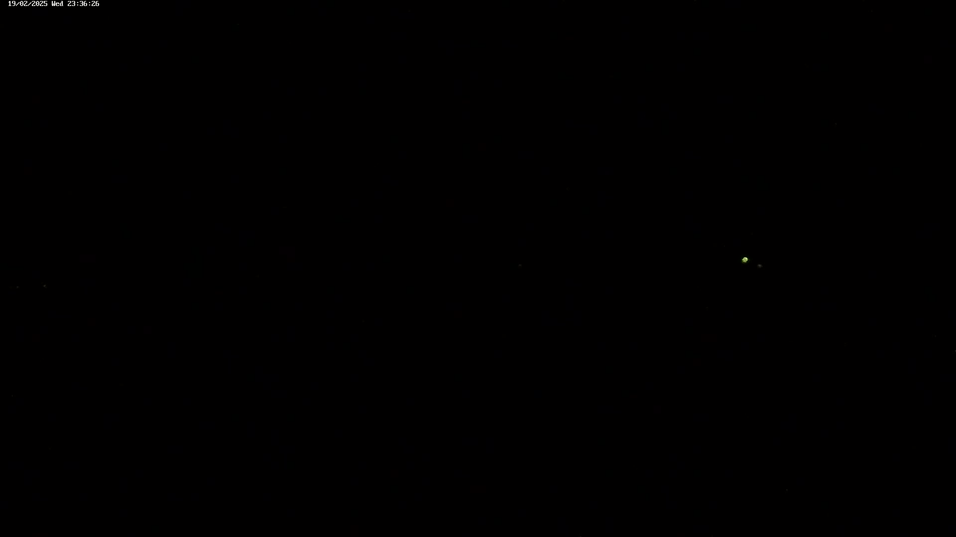 A nighttime image shows a few faint lights in the distance against a completely dark background.