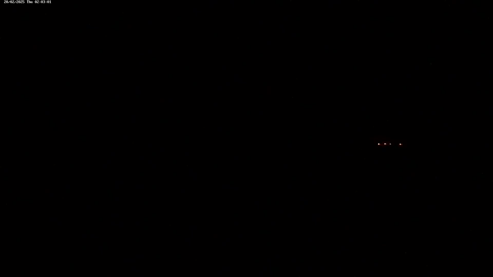 At night, three small red lights are visible in the distance against a completely black background.