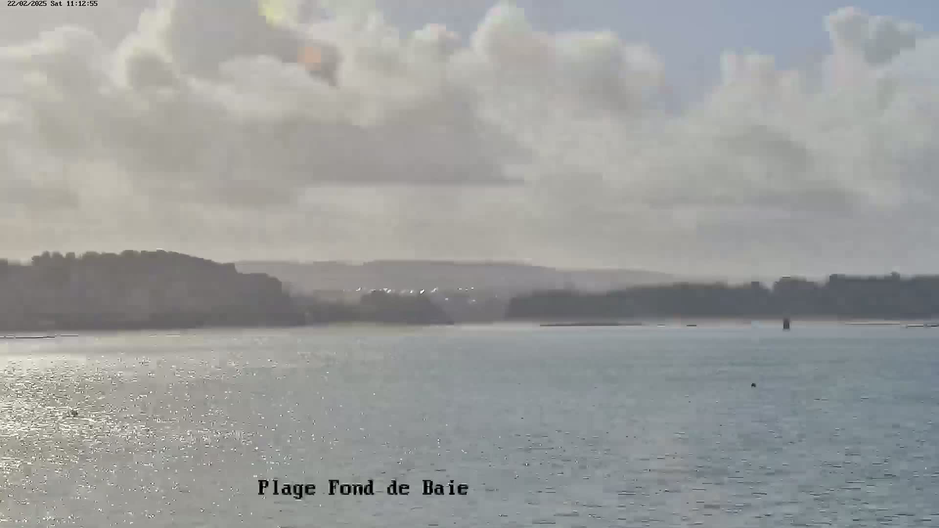 A mostly cloudy day shows a calm body of water with a distant shoreline.