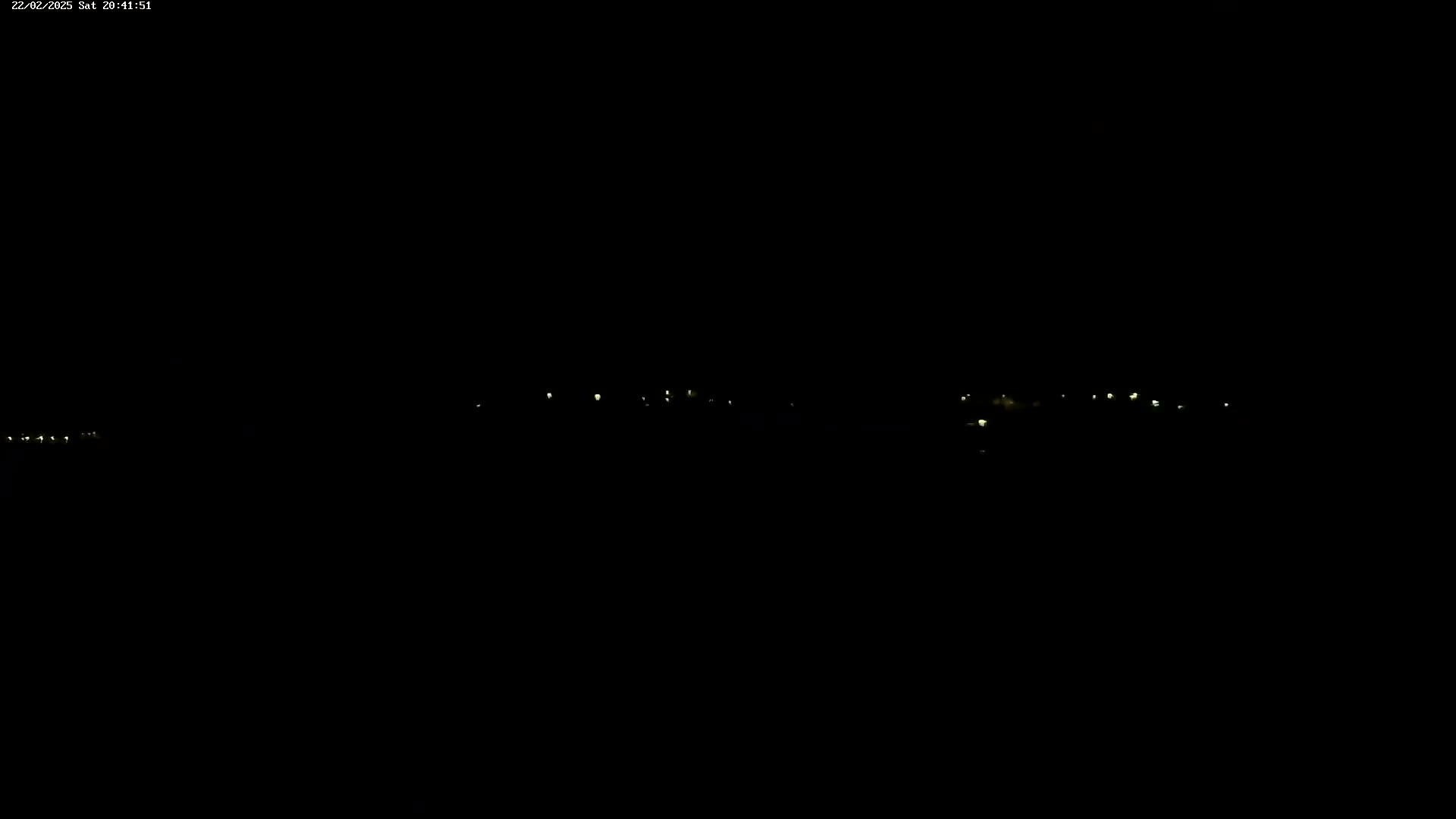 A nighttime long shot shows a few small clusters of faint, distant lights against a completely dark sky.