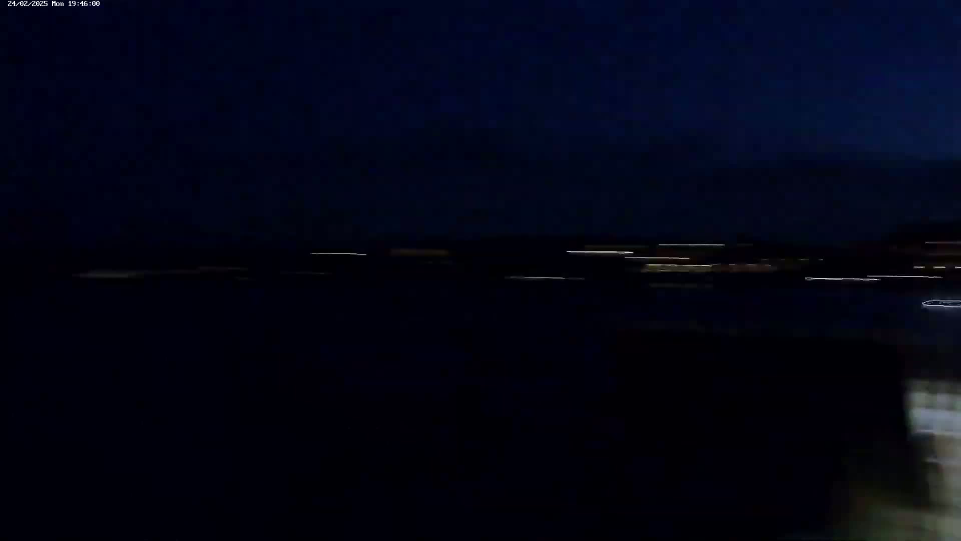 A dark, nighttime scene shows a body of water with a distant line of lights blurred by motion.