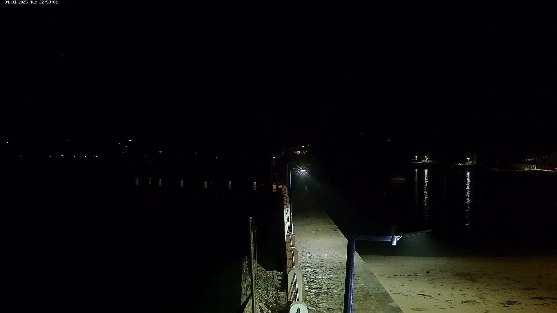 A lighted pier extends into dark water at night, with faint lights visible across the water.