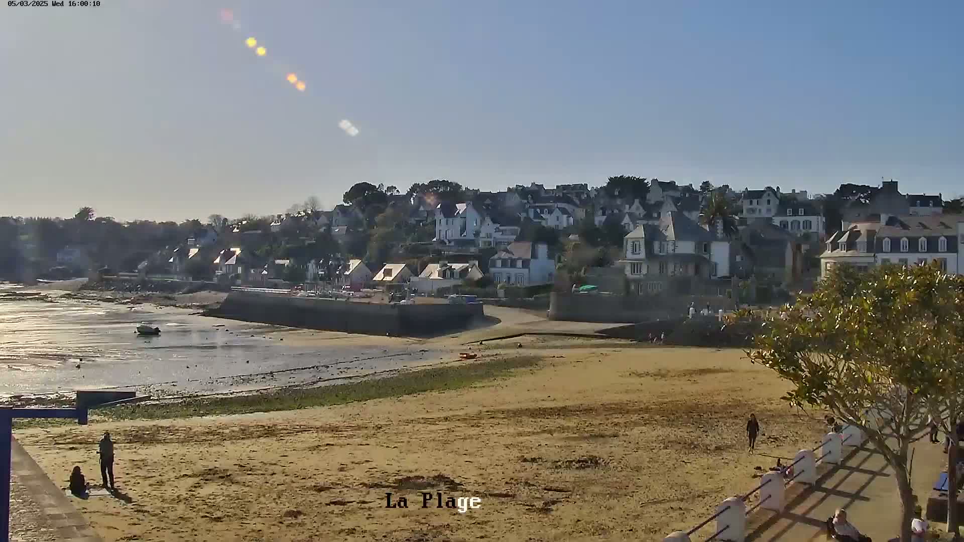 A sandy beach stretches toward a small town of white and gray houses under a mostly sunny sky.