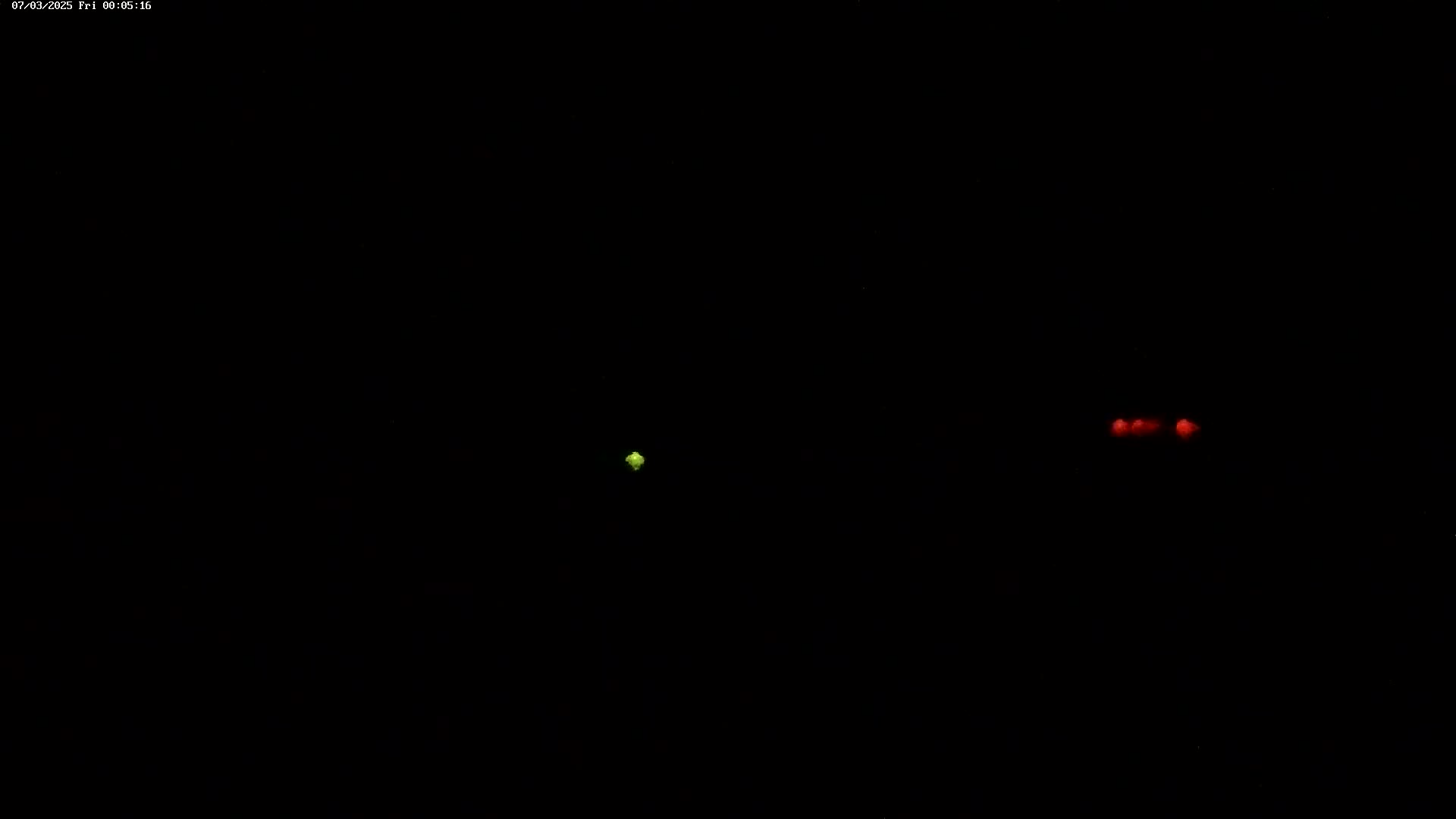 A single small green light and two small red lights are visible in the inky blackness of night.