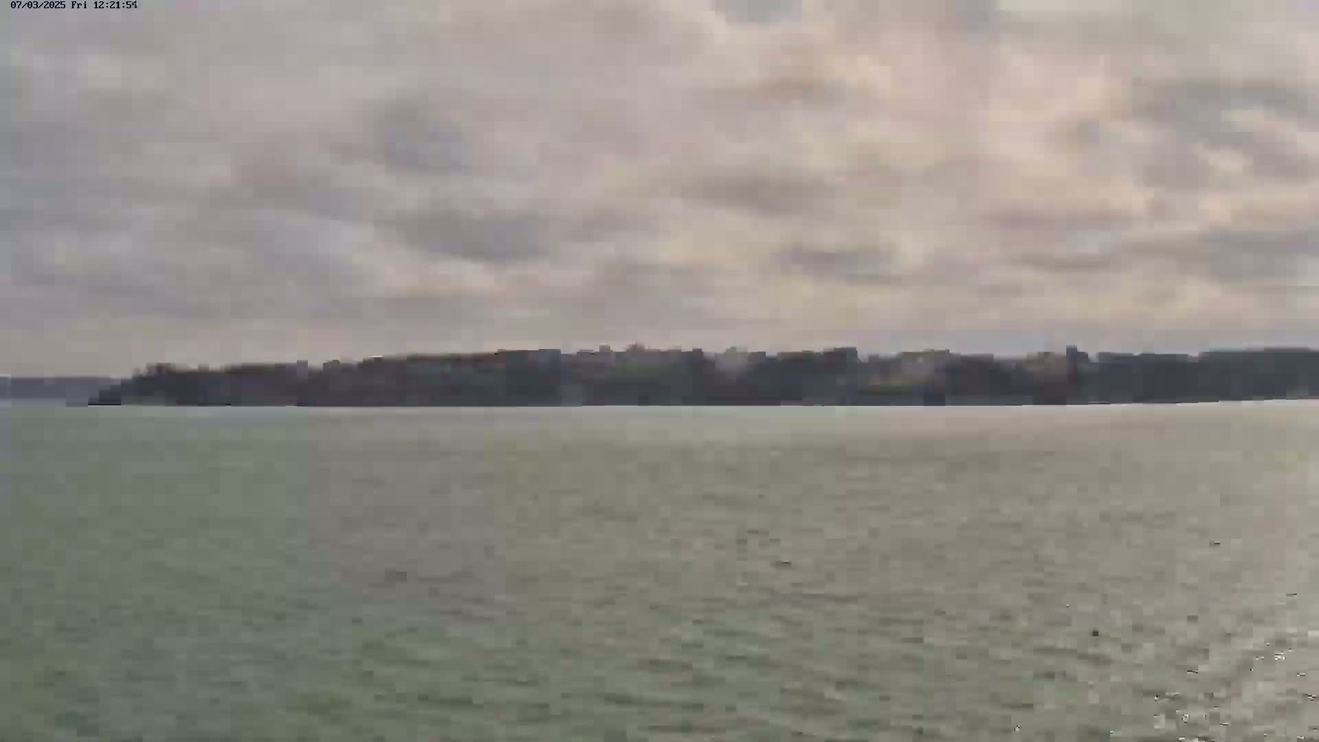 A body of water stretches toward a distant shoreline with overcast skies.