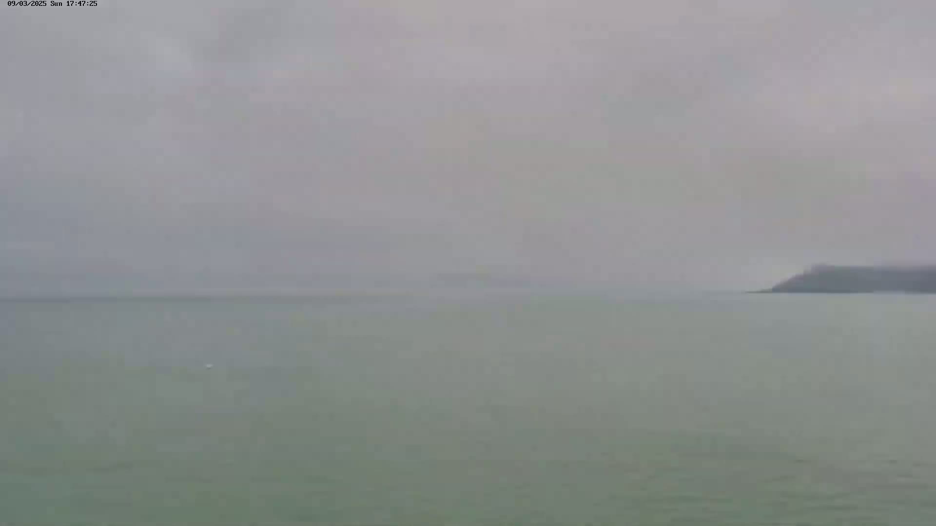 A hazy, overcast day shows a calm body of water with a distant landmass barely visible on the right.