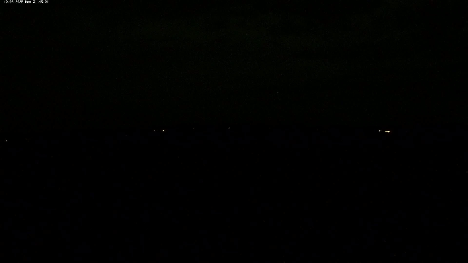 A dark nighttime scene shows a few faint lights in the distance under a mostly clear sky.