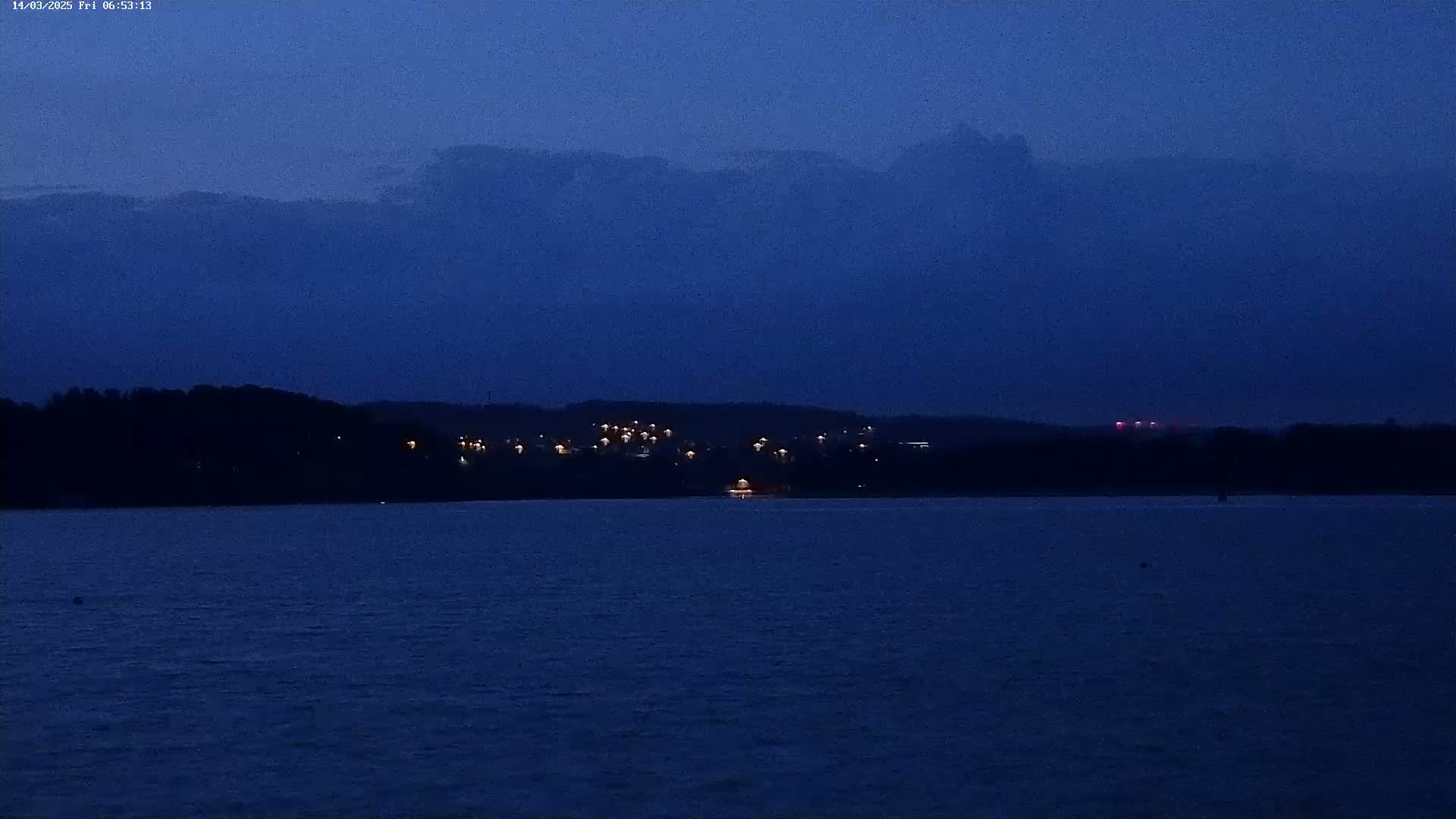A dark blue body of water stretches out before a distant shoreline with sparsely lit buildings under a twilight sky.