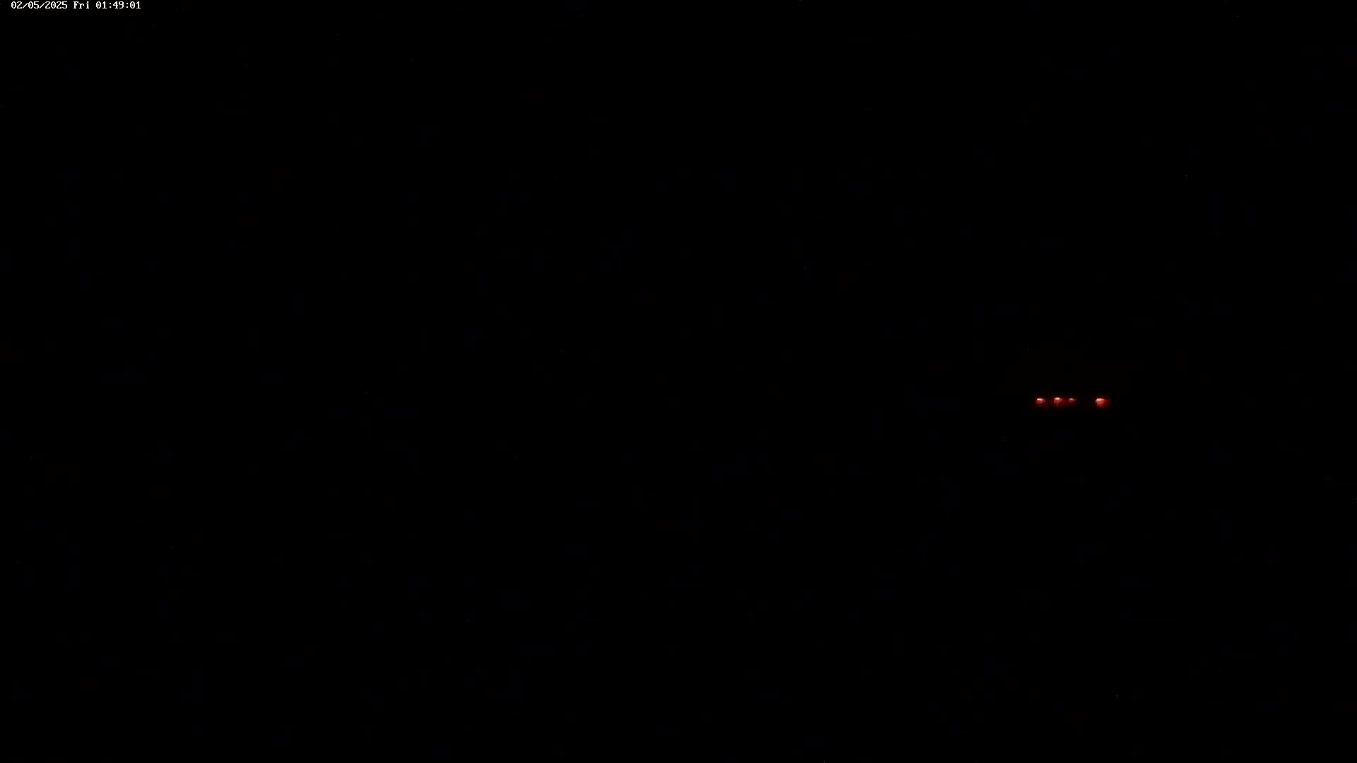 A dark, nighttime scene shows a few small red lights in the distance.