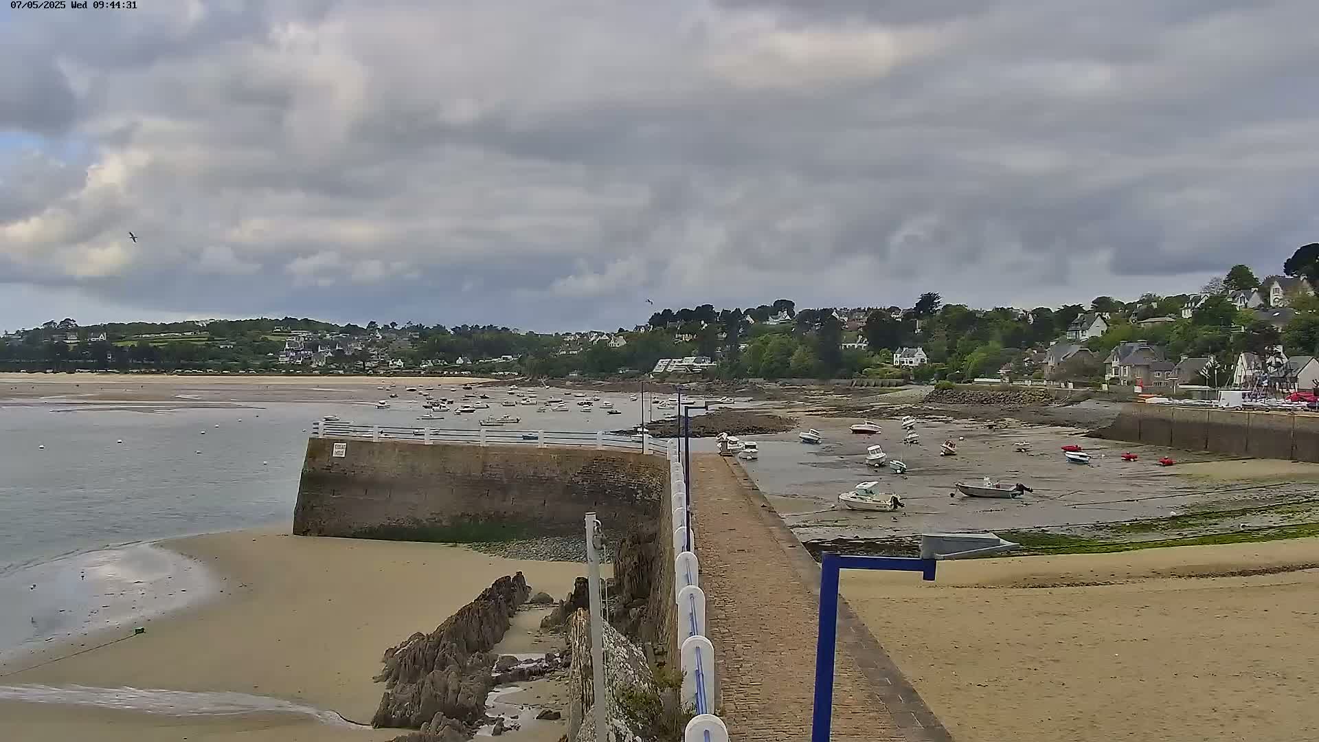 A sandy beach and small harbor filled with numerous boats are visible under a cloudy sky.
