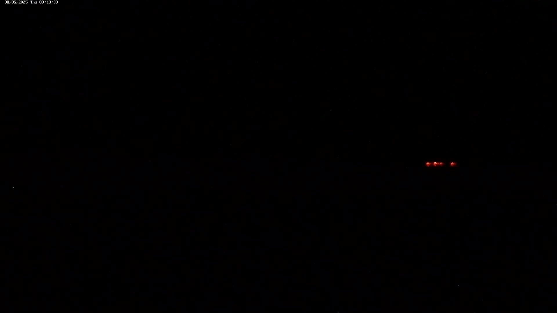 A cluster of faint red lights is visible in the distance against a completely black nighttime sky.