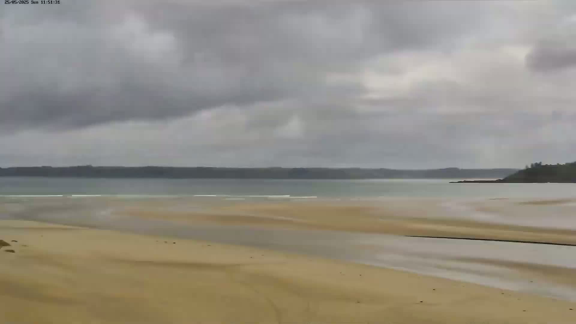 A sandy beach stretches towards a calm bay under an overcast sky.