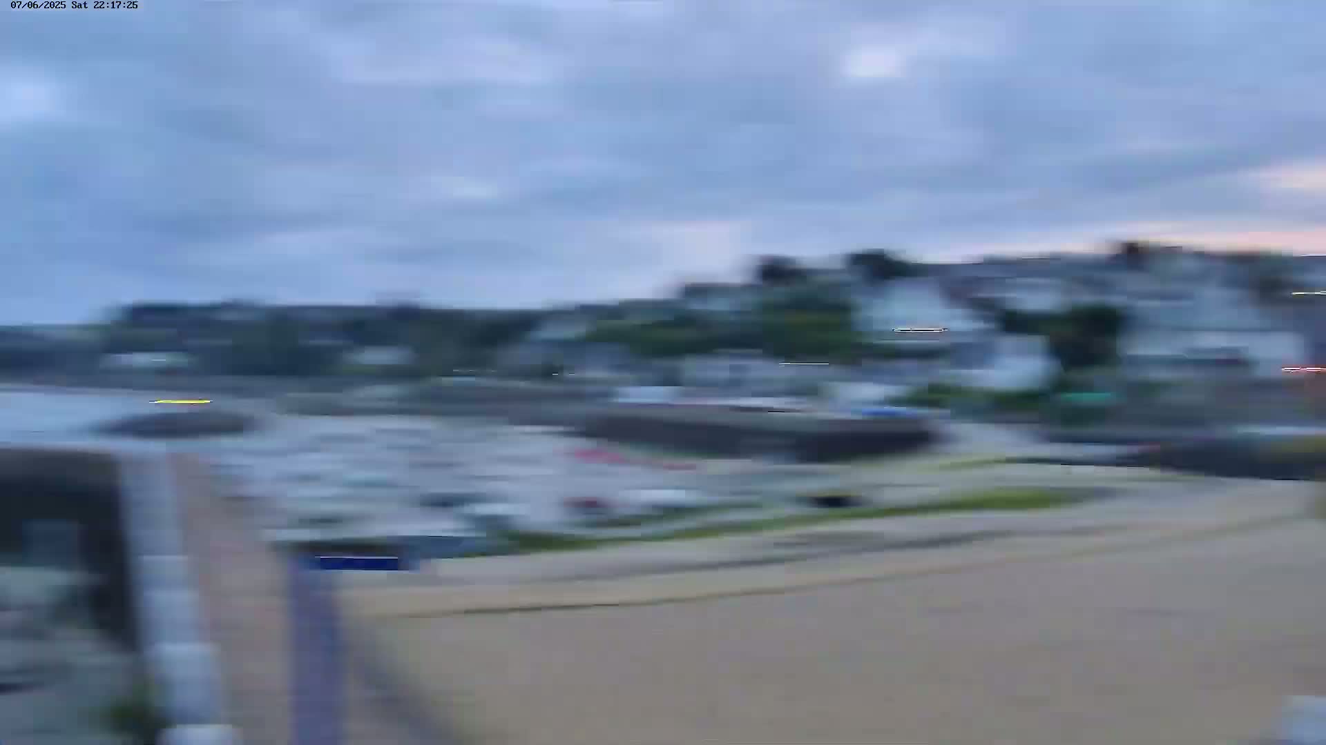 A blurry view of a harbor filled with boats, overlooked by a town under an overcast sky.