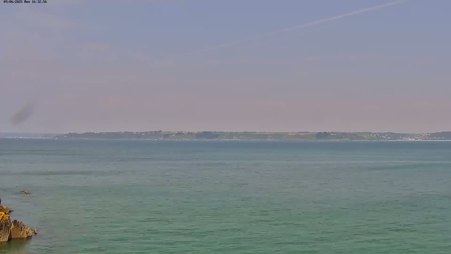 A calm, hazy day shows a body of water with a distant shoreline visible across the expanse of the sea.