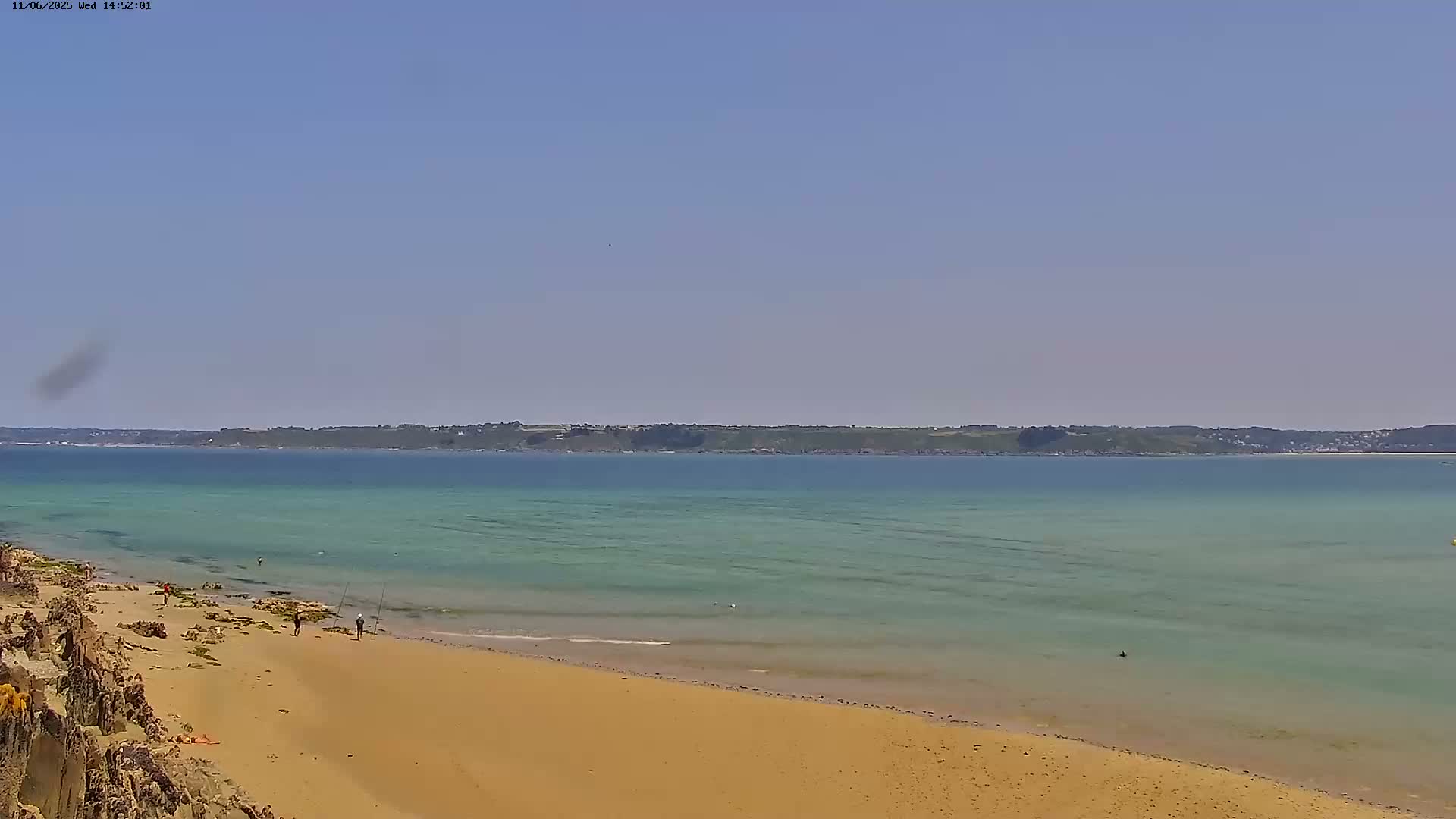 A sandy beach slopes down to a calm, light-green ocean under a clear blue sky.