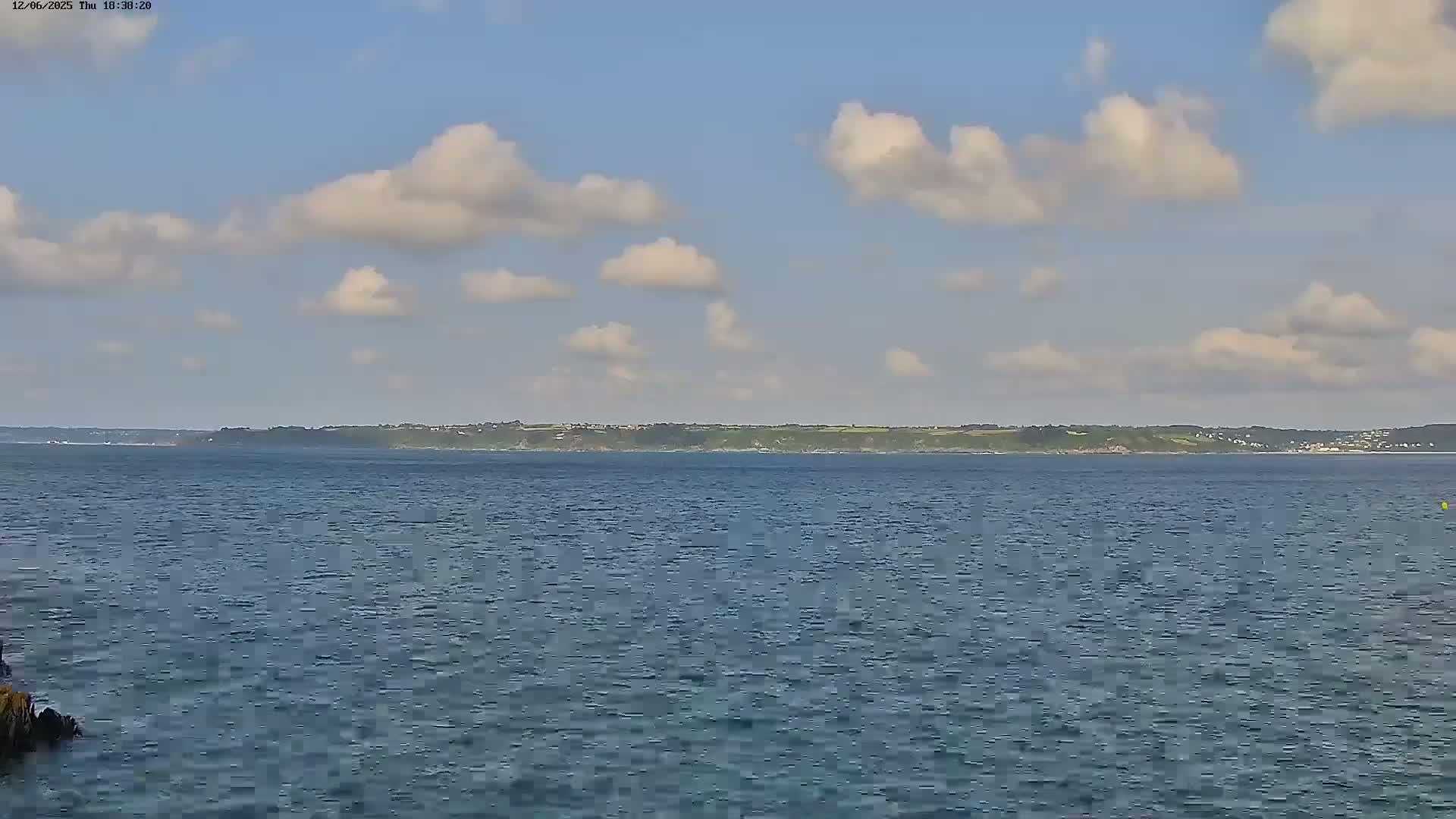 A calm body of water stretches toward a distant coastline under a partly cloudy sky.