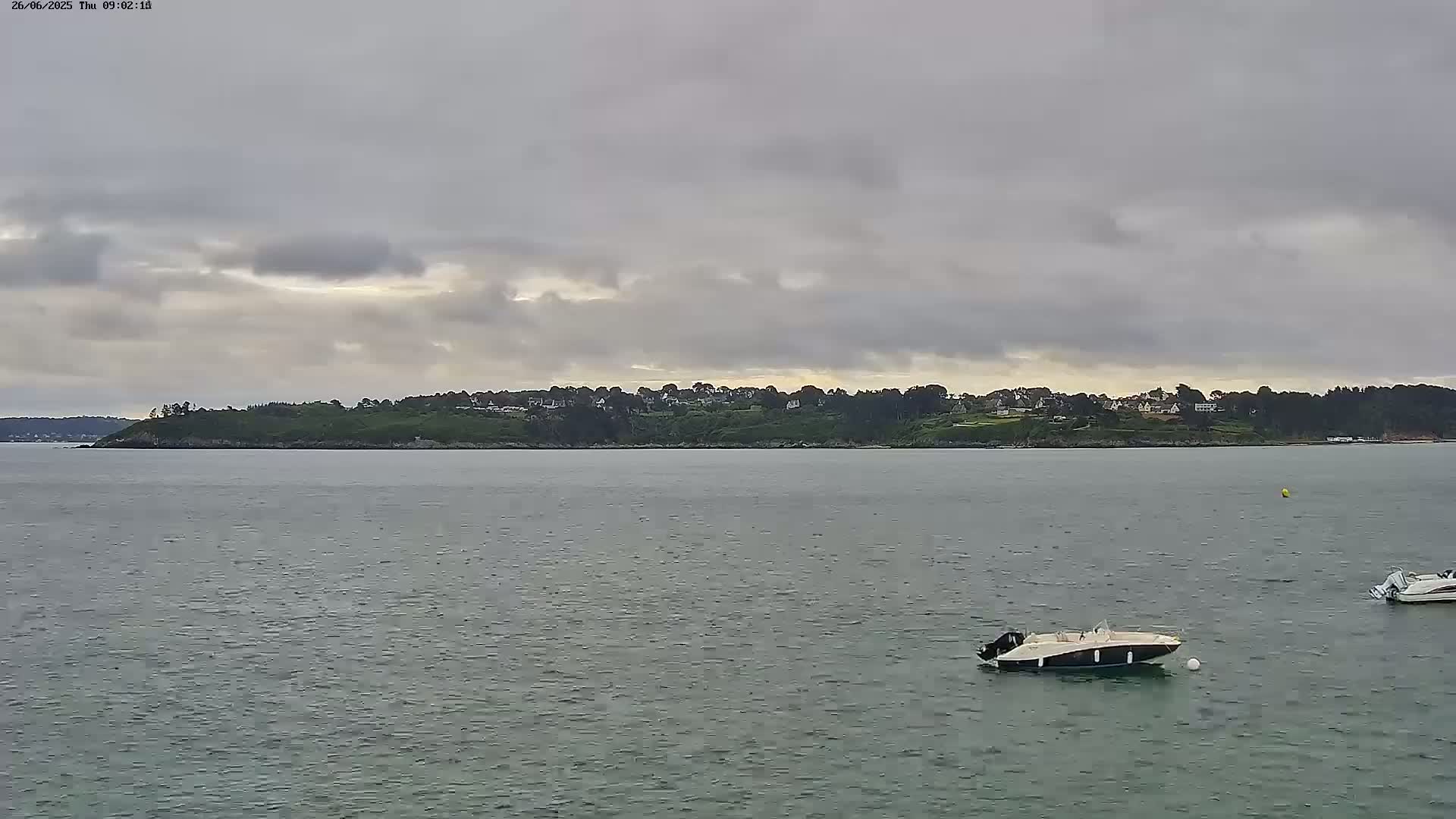Two motorboats are on a calm, gray day on a body of water in front of a tree-covered shoreline with houses.