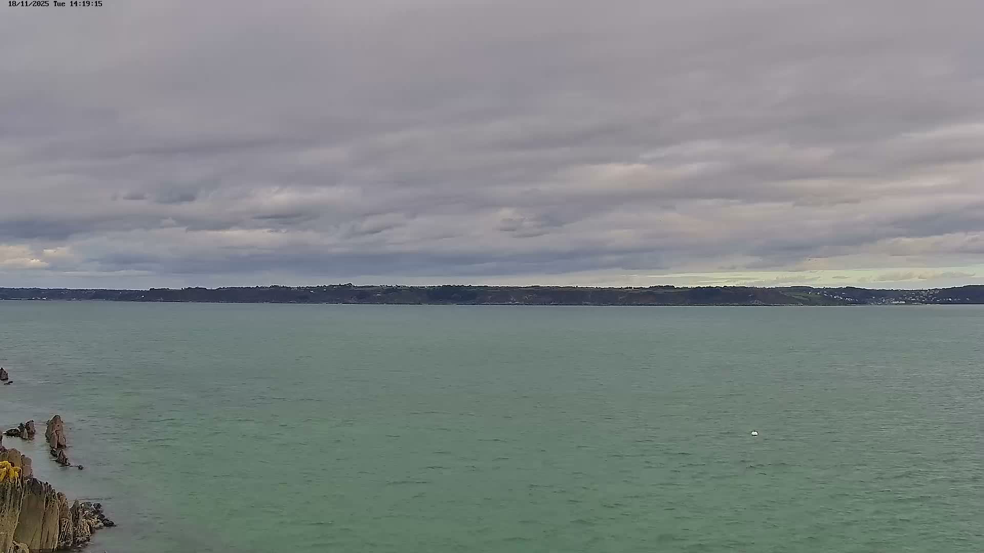 A calm, overcast day at a coastal town, with small waves lapping the shore and two small boats moored in the water.