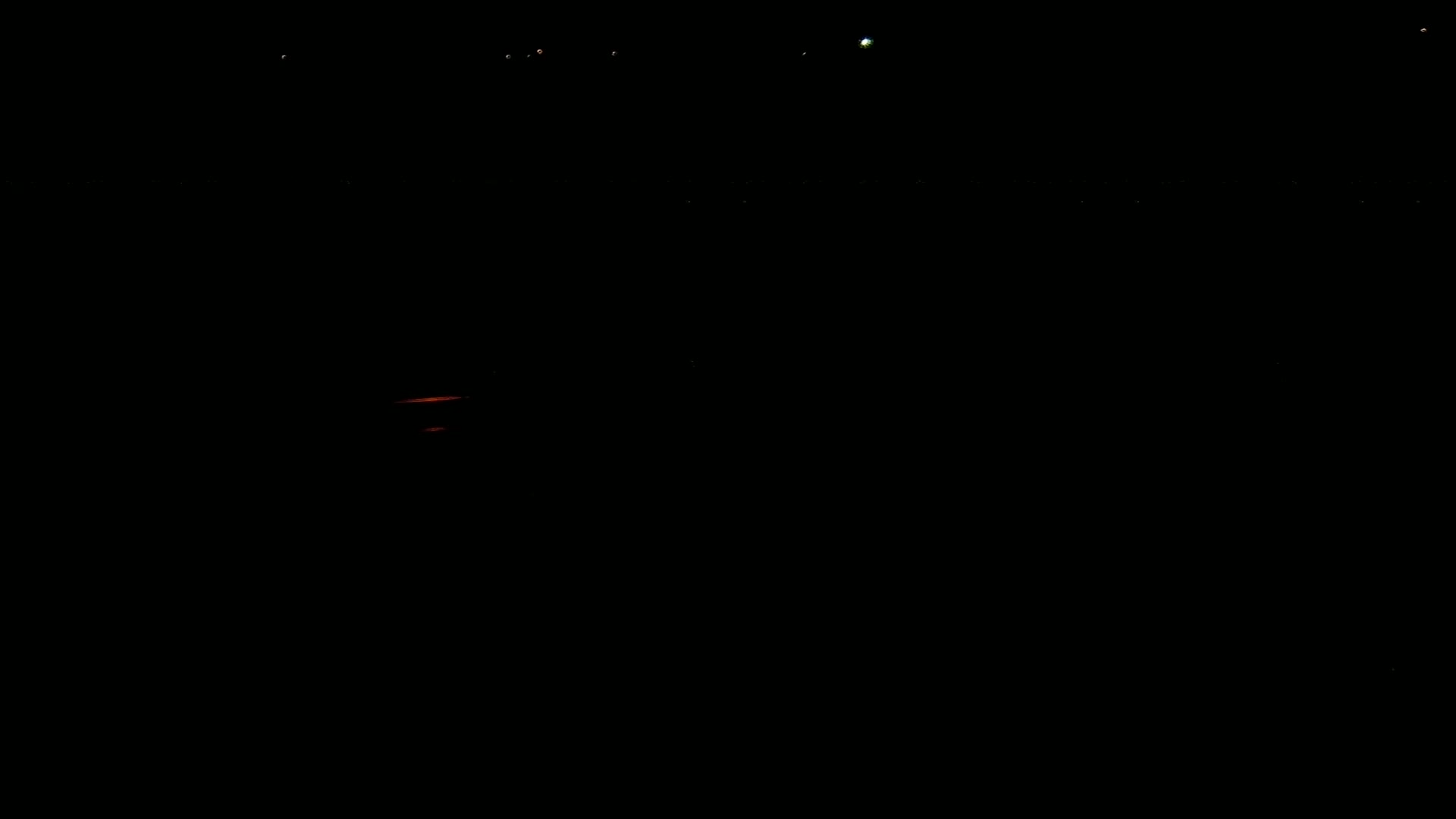 A dark nighttime scene shows a few distant lights and a faint orange glow near the bottom.