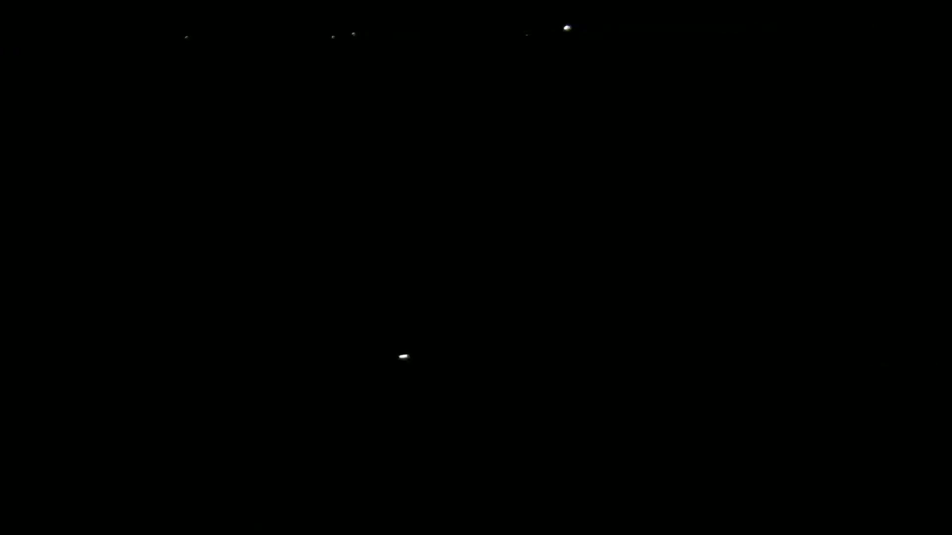 A dark scene at night shows several faint points of light in the distance.