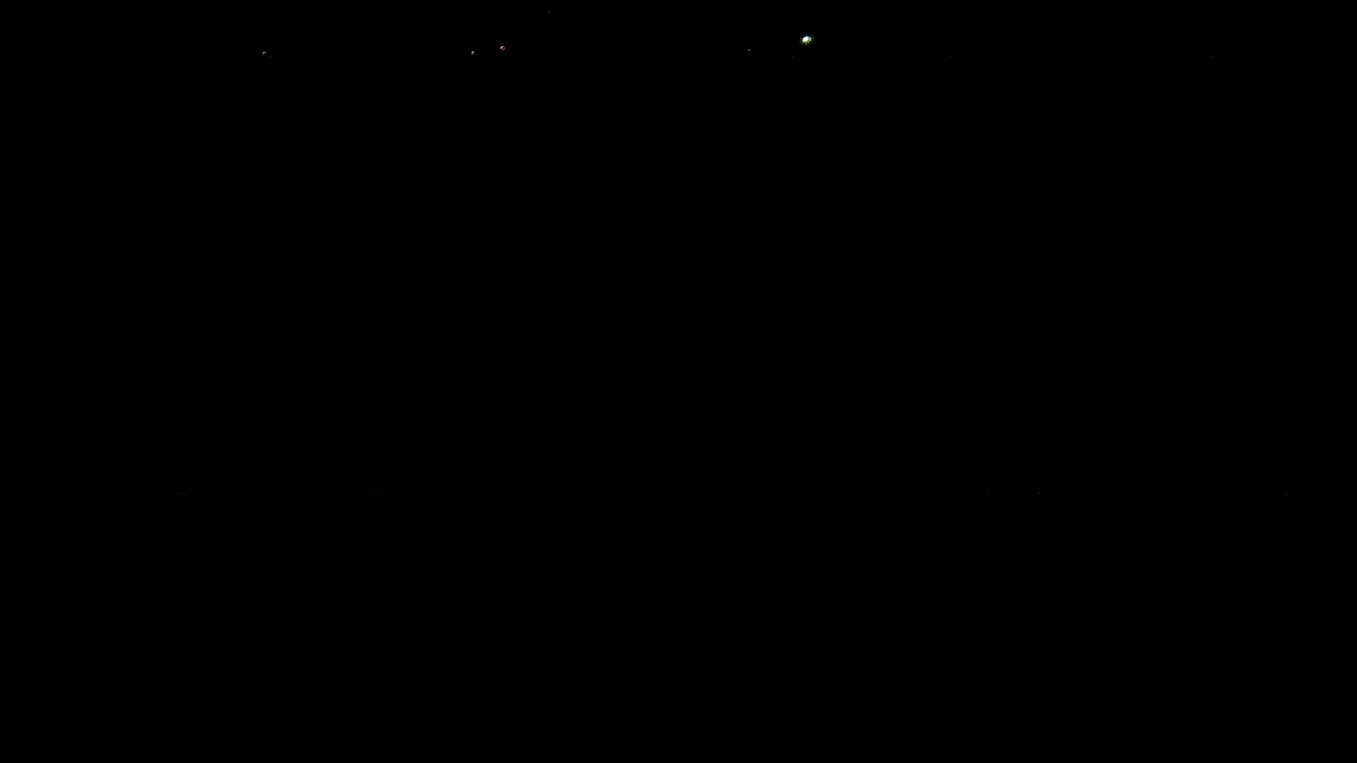 A dark, night scene shows several faint lights in the distance.