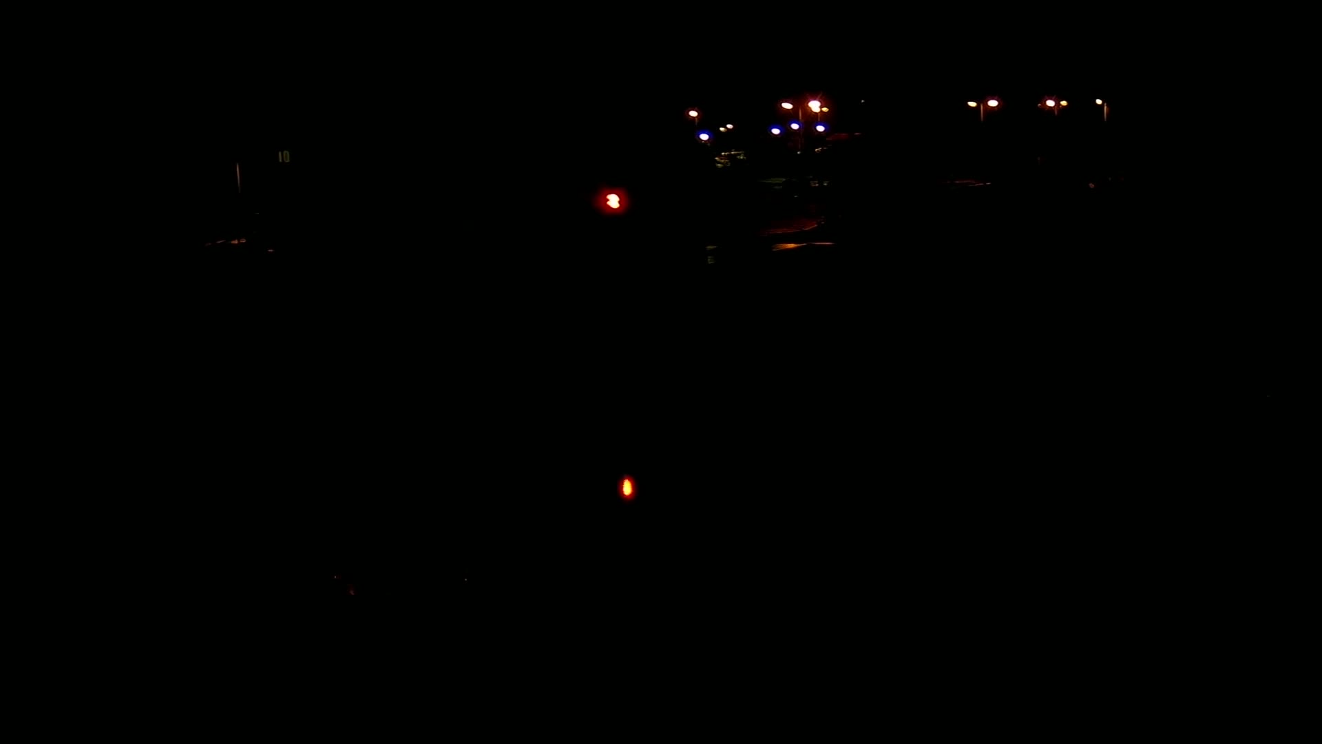 At night, a few distant lights illuminate a dark road with a few red and white lights visible closer to the viewer.