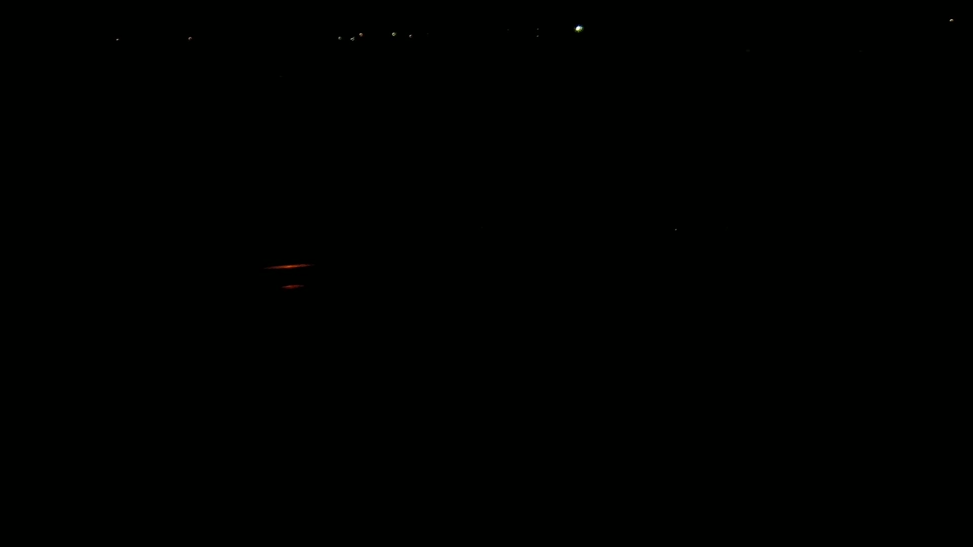 At night, two faint orange lights are visible in the distance, with several brighter lights higher up in the dark sky.