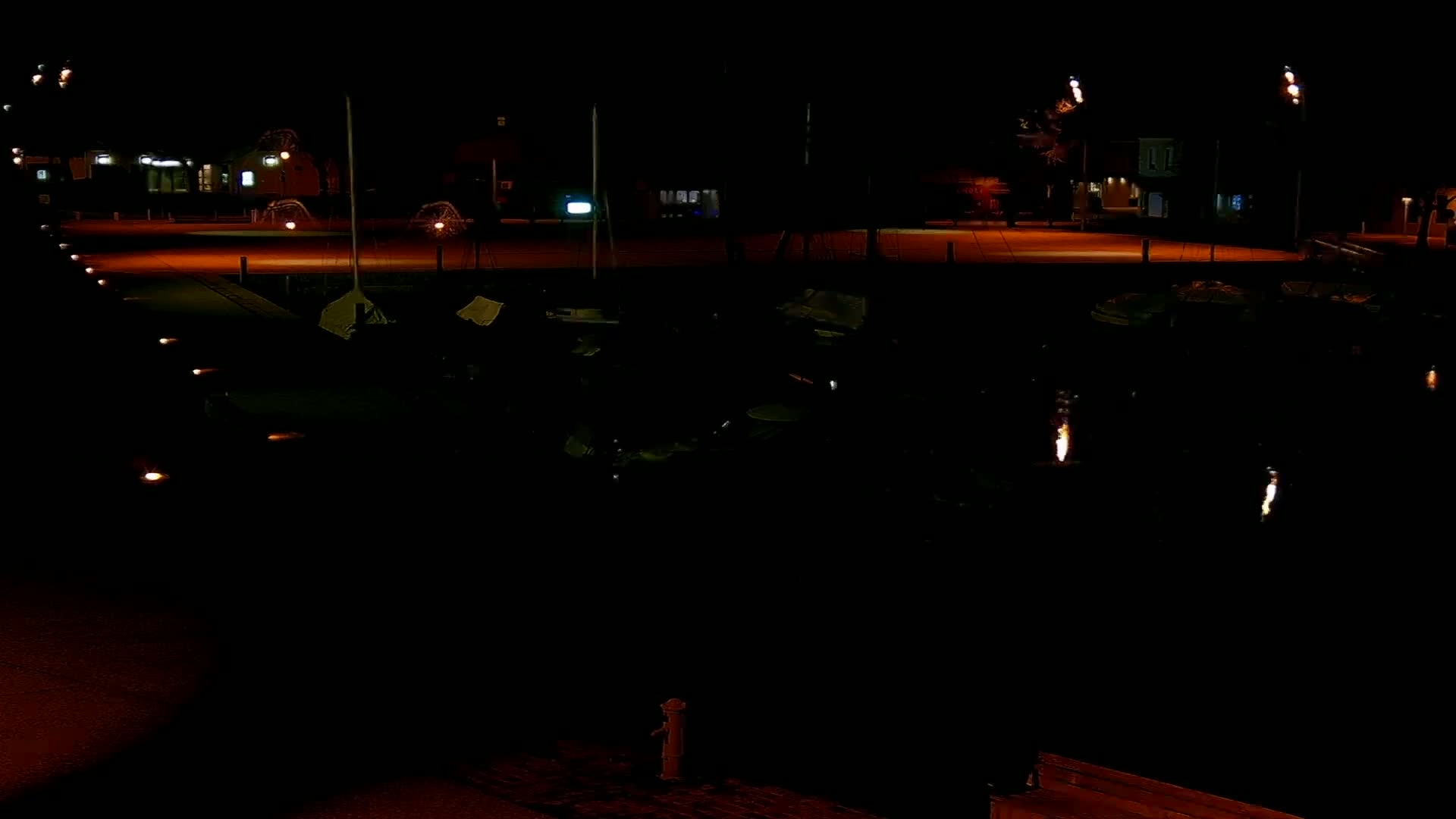 A nighttime view of a dark body of water reflecting lights from a nearby, sparsely lit waterfront area.