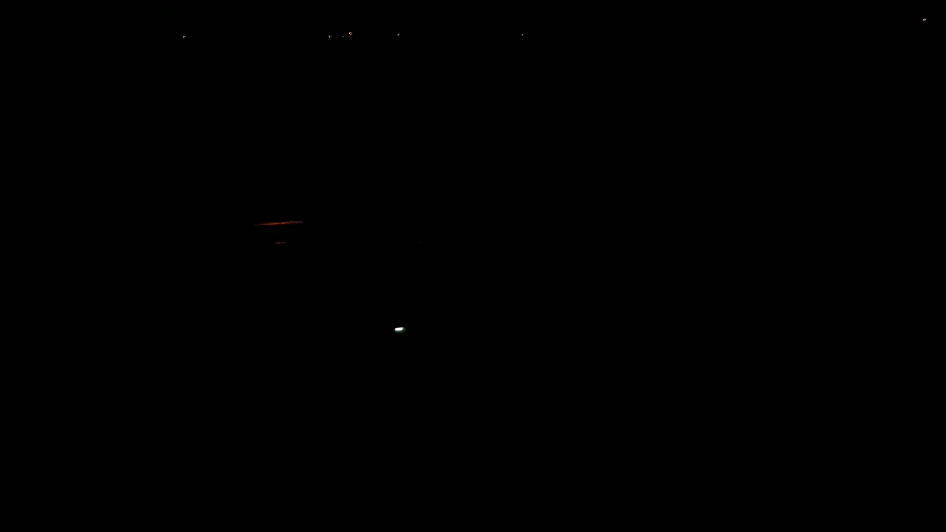 A dark scene at night shows a few faint lights in the distance and a small bright light closer to the viewer.