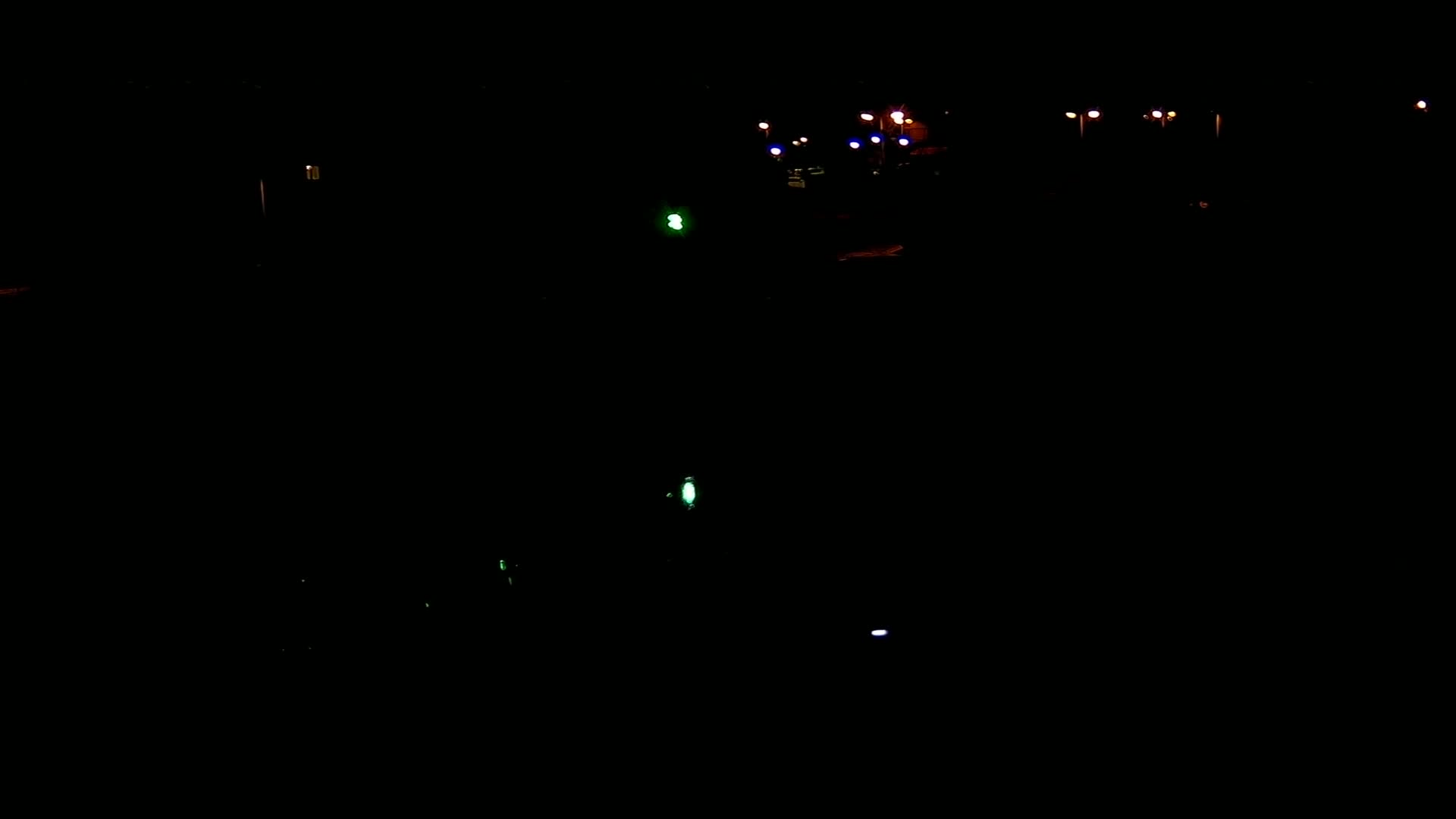 A mostly dark nighttime scene shows a few scattered lights from what appears to be a road or parking lot.
