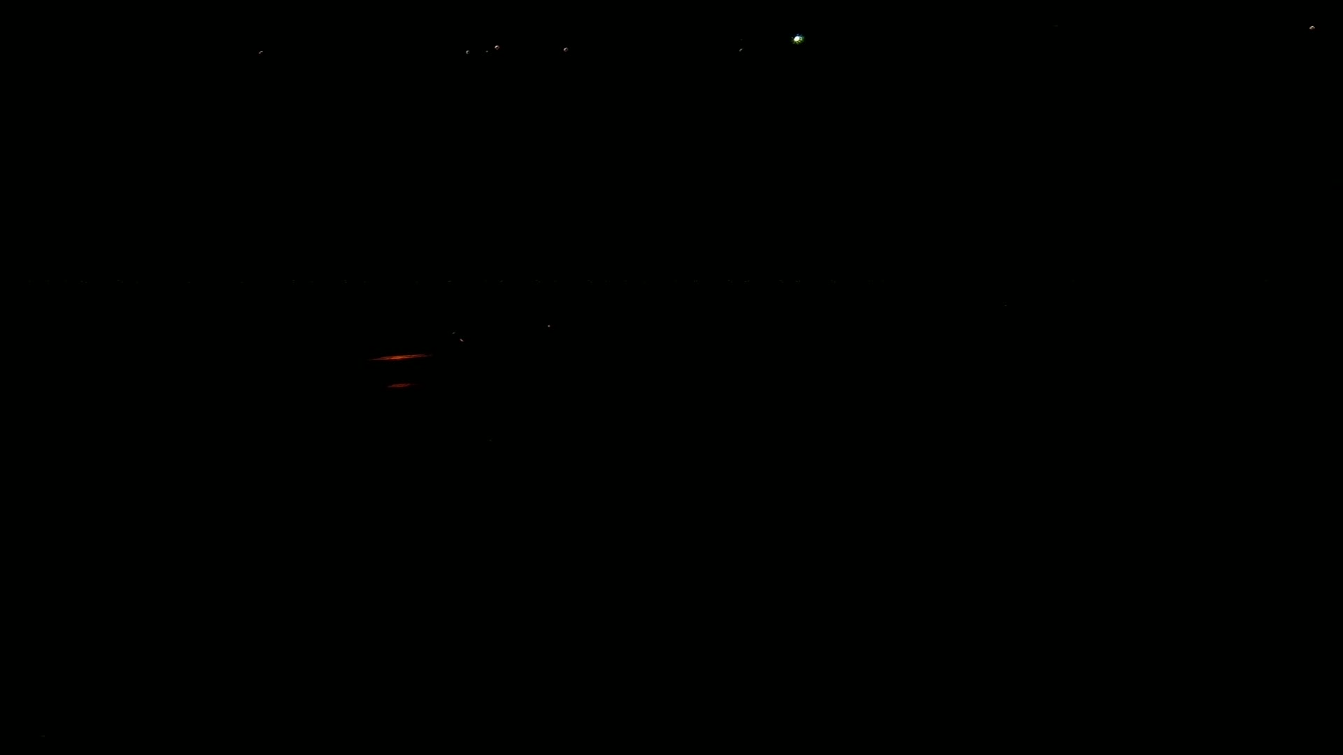 A dark scene at night shows a few distant lights and a faint orange glow near the bottom.