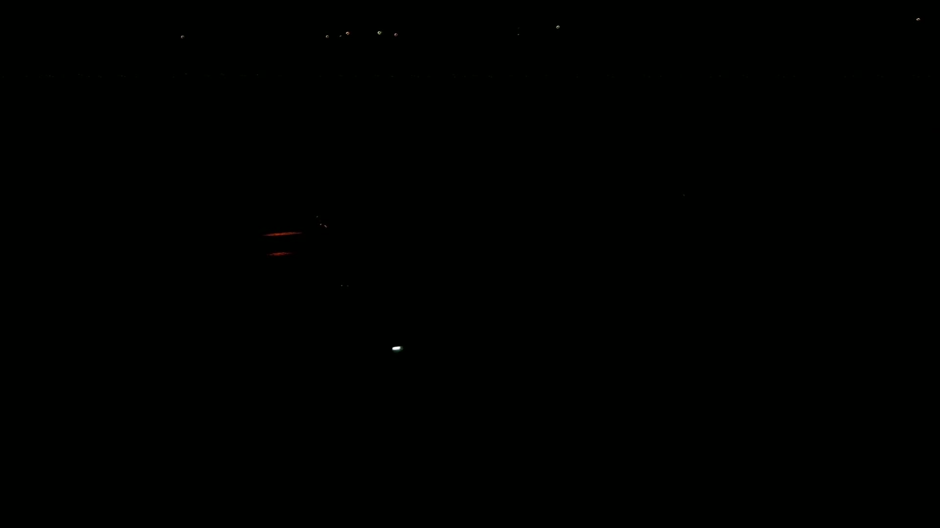 A dark night scene shows a few distant lights and two faint reddish lights closer to the bottom of the frame.