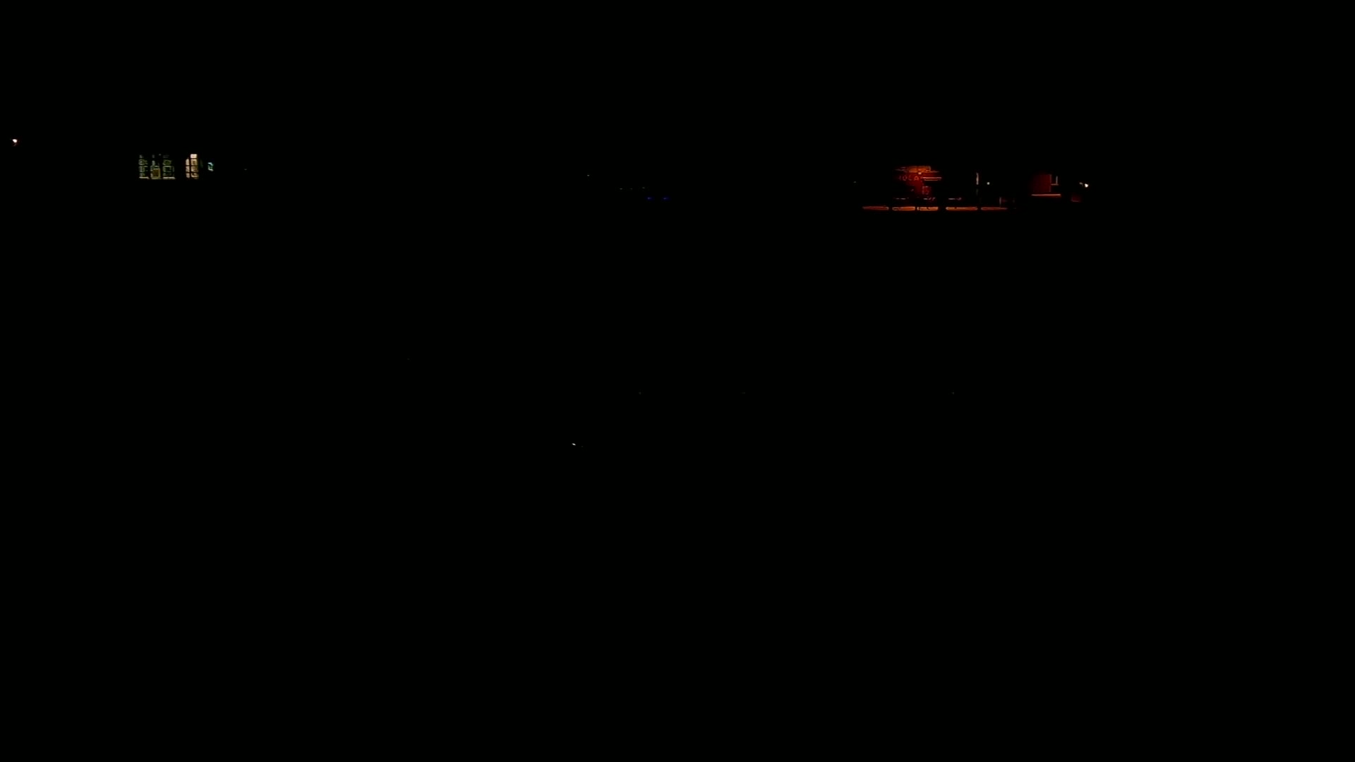 Dimly lit buildings are visible at night in the distance.