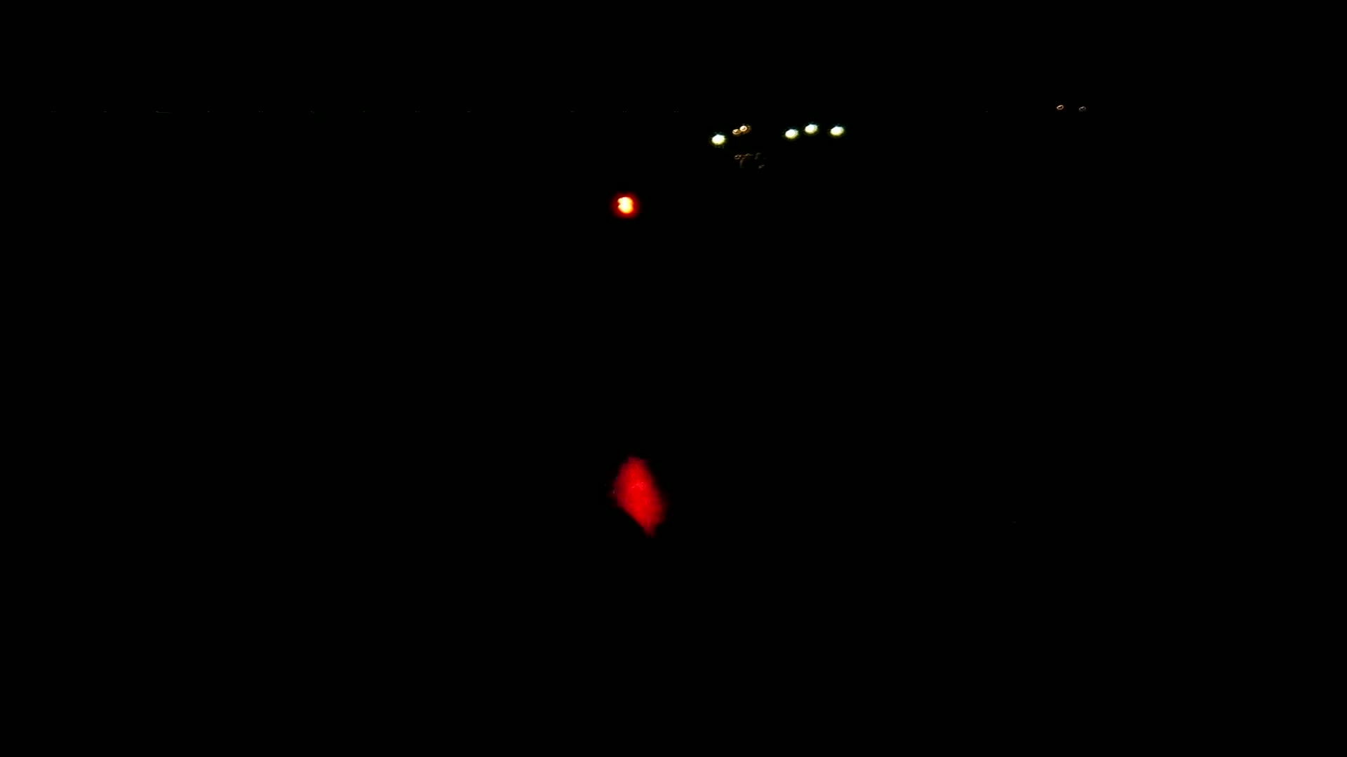 A dark, nighttime scene features several small, distant lights, including one red light closer to the viewer.