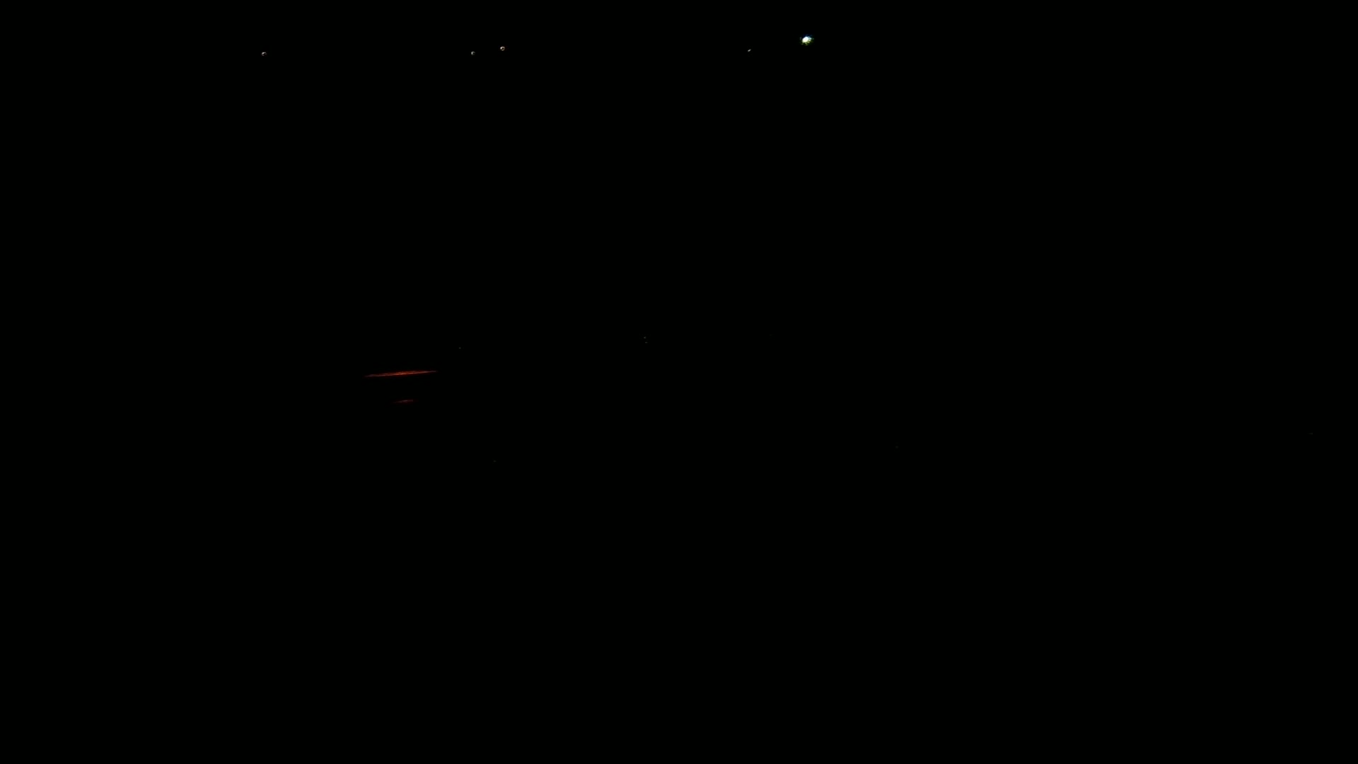 A dark, nighttime scene shows a faint orange glow near the bottom and a few distant, bright lights.
